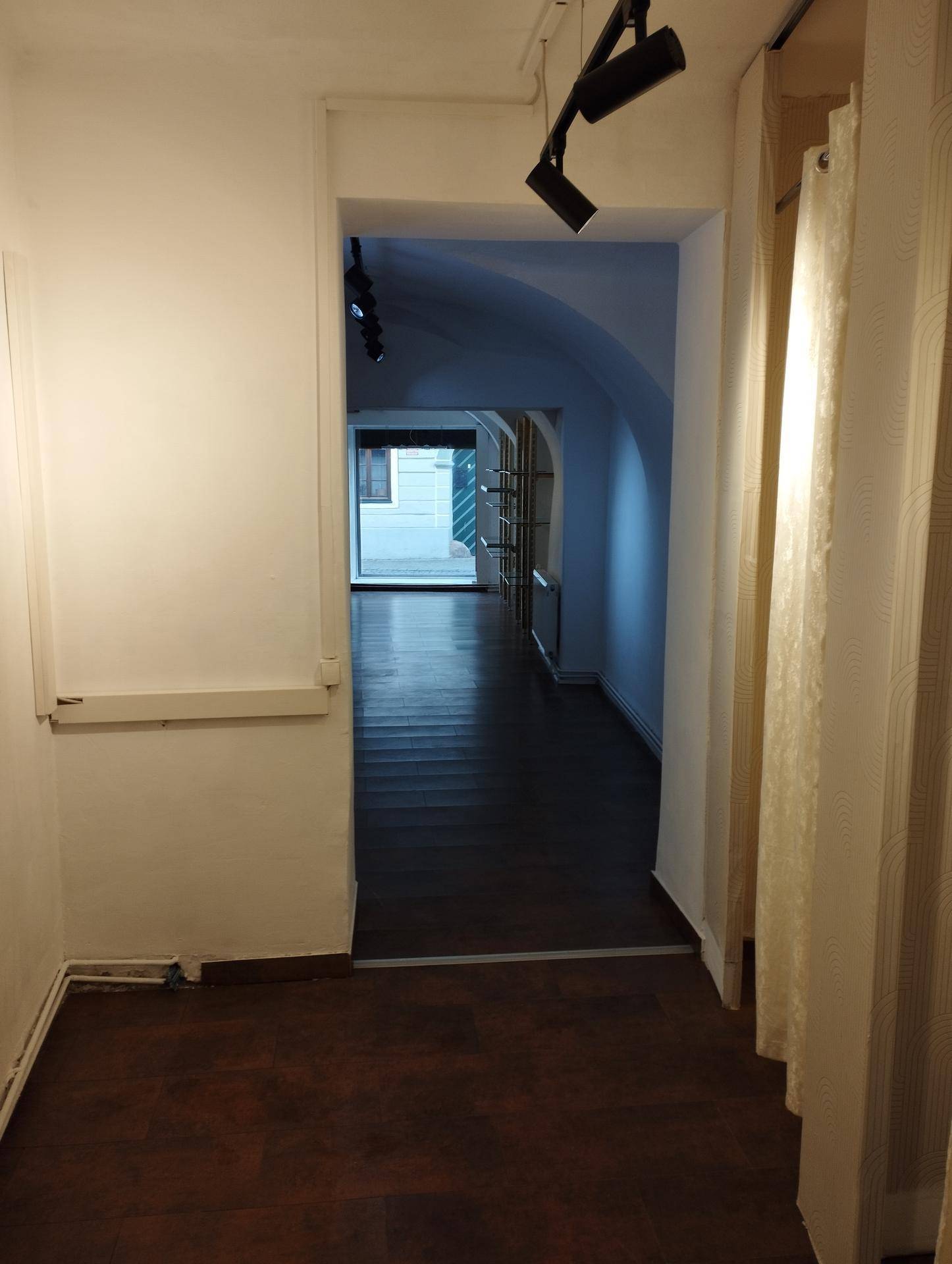 Langer Flur mit dunklem Holzboden und gewölbten Decken, der zu einem weiteren Raum mit Fenster führt.