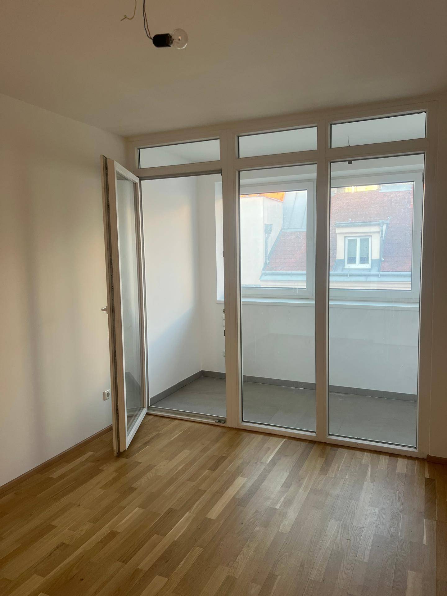 Helles Zimmer mit Holzboden und Zugang zu einem verglasten Balkon oder Wintergarten.