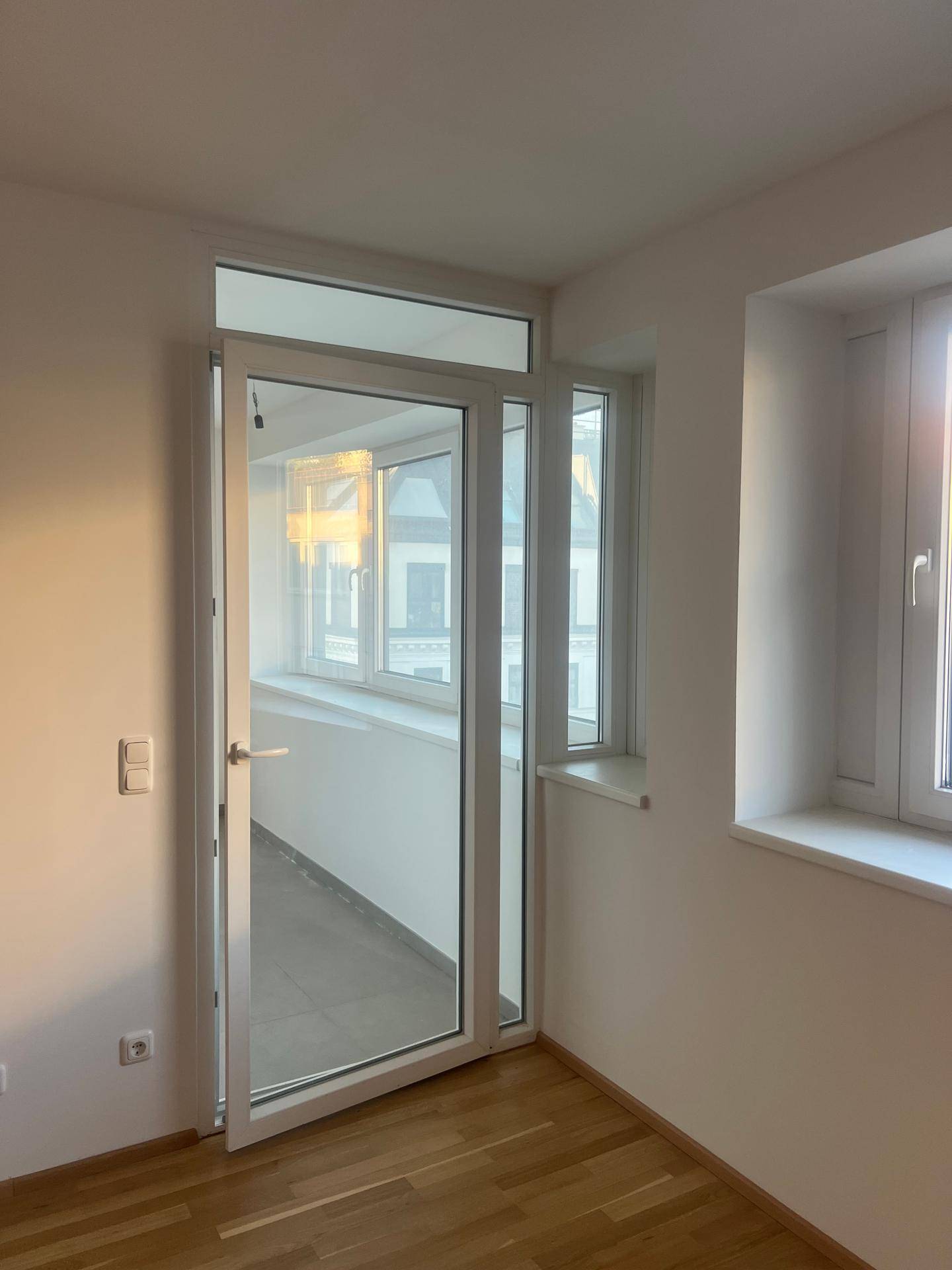 Helles Zimmer mit Holzboden und zwei Fenstern, die viel Tageslicht hereinlassen.