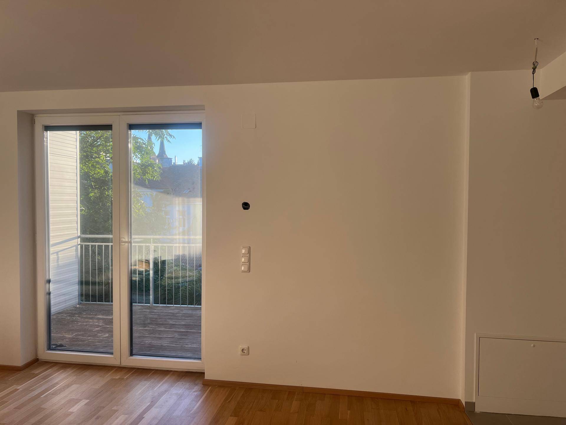 Geräumiges Zimmer mit Holzboden und großen Fenstern, die viel Tageslicht hereinlassen.