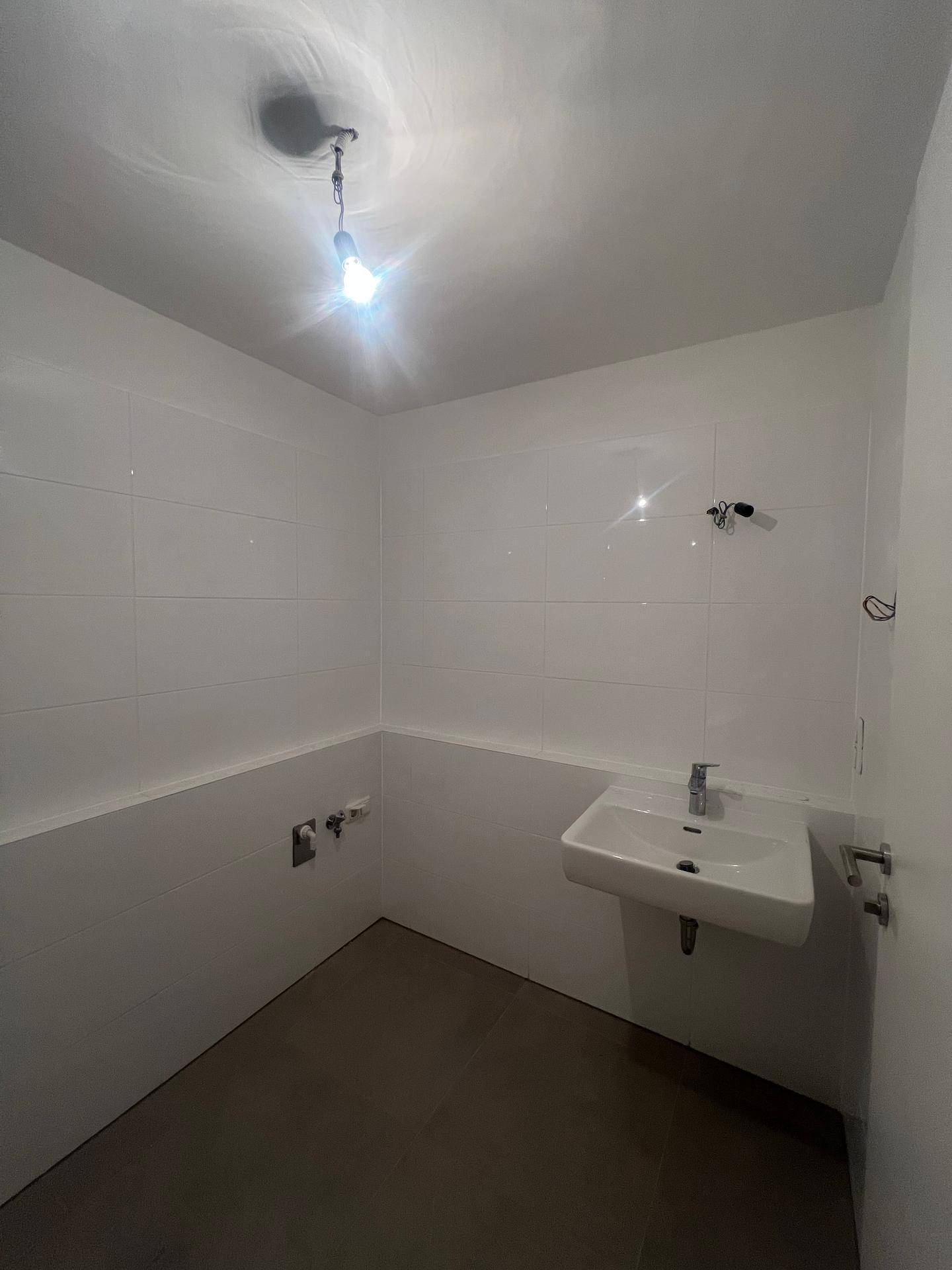 Modernes Badezimmer mit weißen Fliesen, Waschbecken und Vorbereitung für weitere Installationen.
