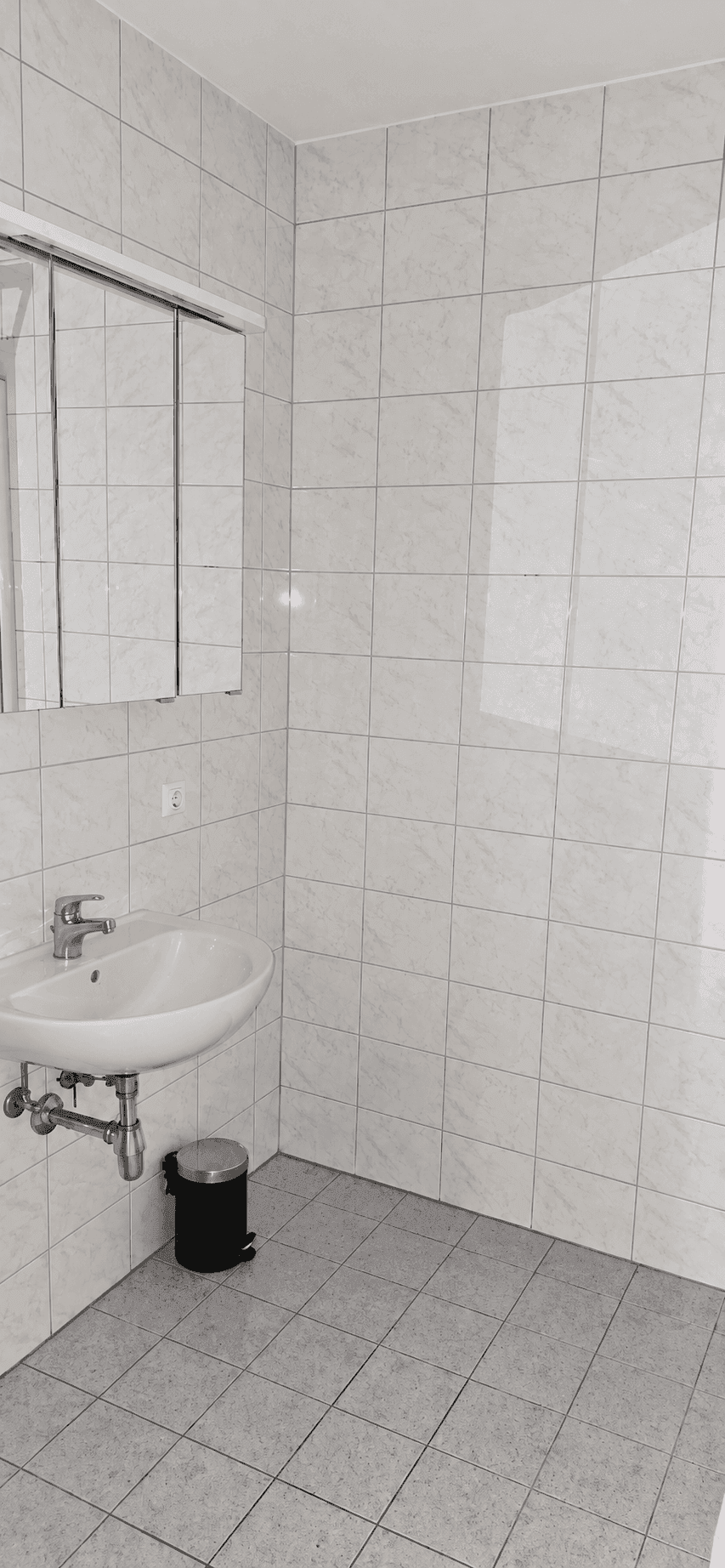 Modernes Badezimmer mit hellen Fliesen, Einzelwaschbecken und Spiegelschrank.