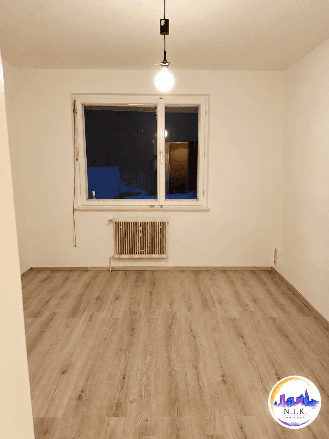 Helles Zimmer mit Laminatboden und Fenster, das viel Tageslicht hereinlässt.