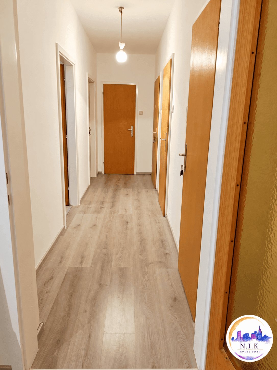 Langer Flur mit hellem Laminatboden und mehreren Holztüren, der zu verschiedenen Räumen führt.