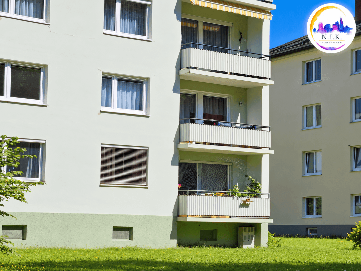 Mehrfamilienhaus mit hellgrüner Fassade, mehreren Balkonen und gepflegter Grünfläche.