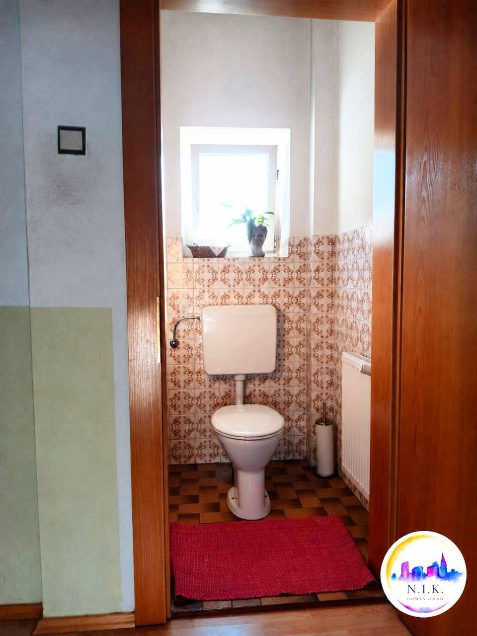Kleines Gäste-WC mit Fenster, gemusterten Wandfliesen und einem einfachen Stand-WC.