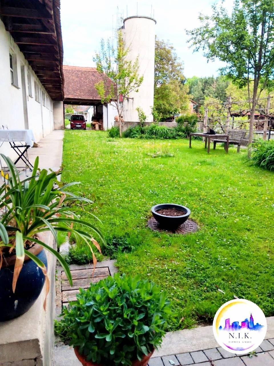 Großer grüner Garten mit Rasenfläche, Bäumen und einem ländlichen Ausblick im Hintergrund.