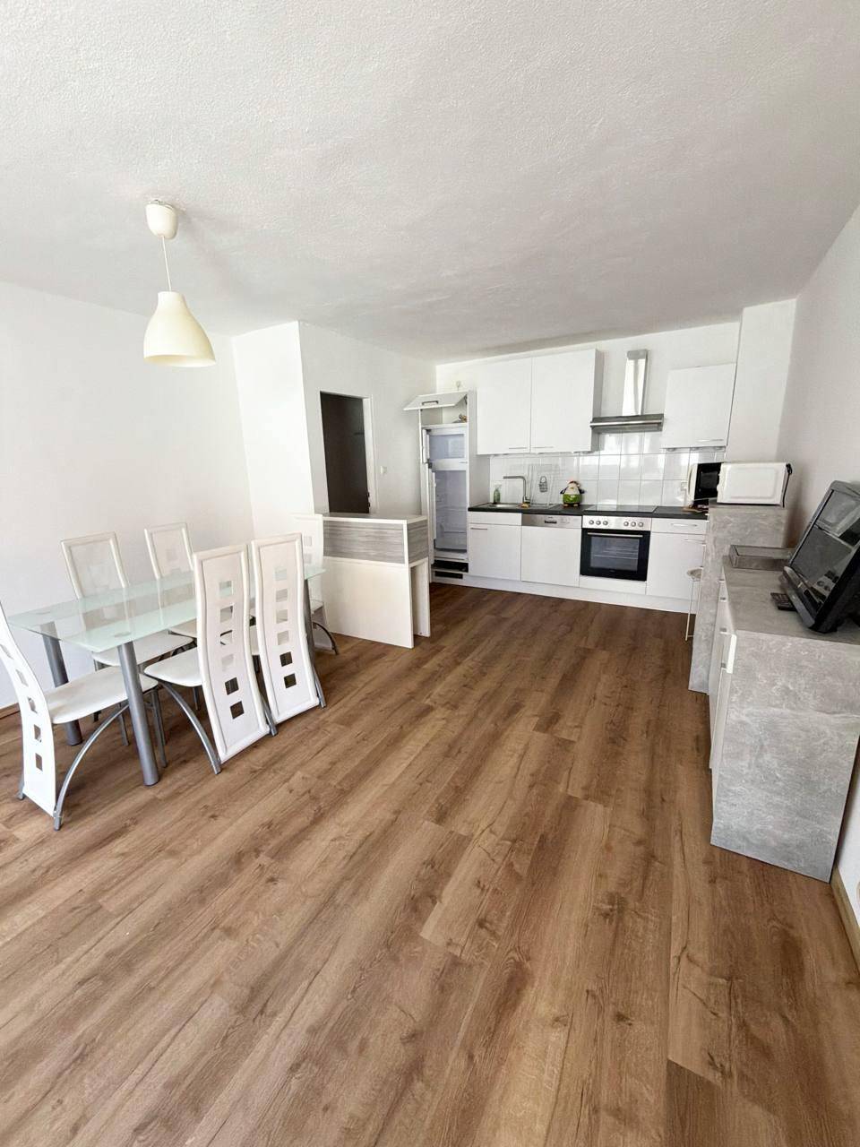 Moderne, offene Küche mit weißen Schränken, Essbereich und Laminatboden in hellem Holzton.