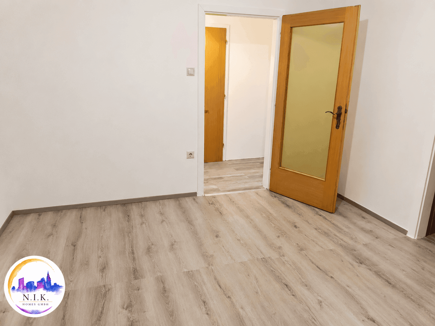 Leeres Zimmer mit hellem Laminatboden und Holztüren, bereit zur individuellen Gestaltung.