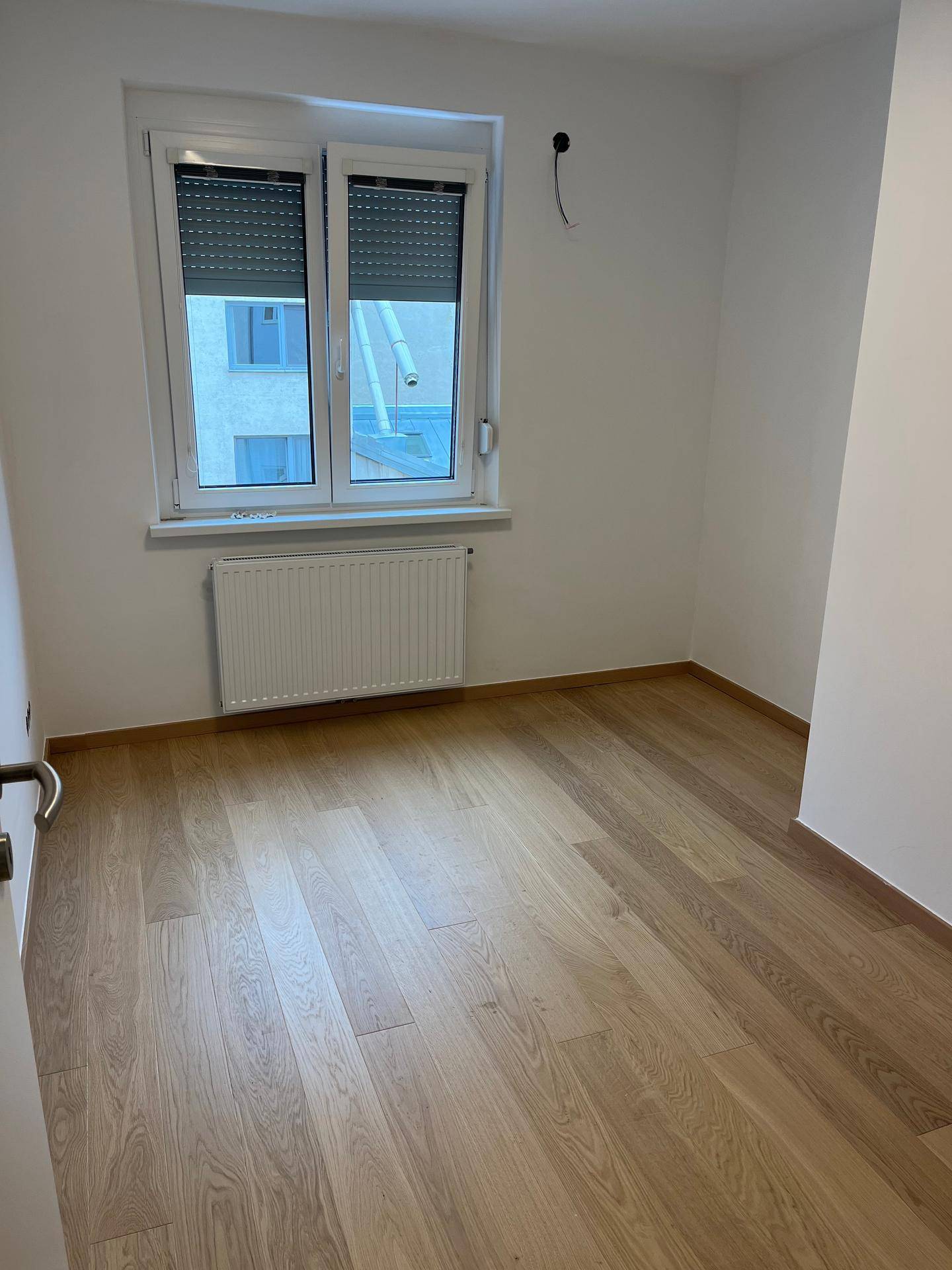 Helles Zimmer mit Parkettboden, Fenster und Heizkörper, ideal als Schlaf- oder Arbeitszimmer.