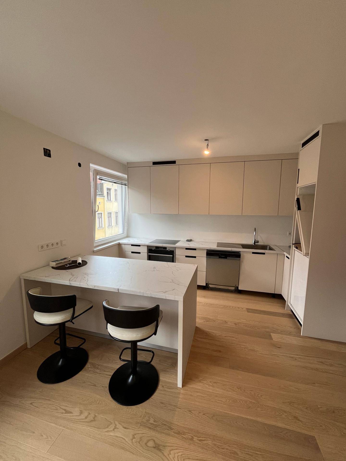 Moderne Einbauküche mit hellen Schränken, integrierten Geräten und einer Kücheninsel mit Barhockern.