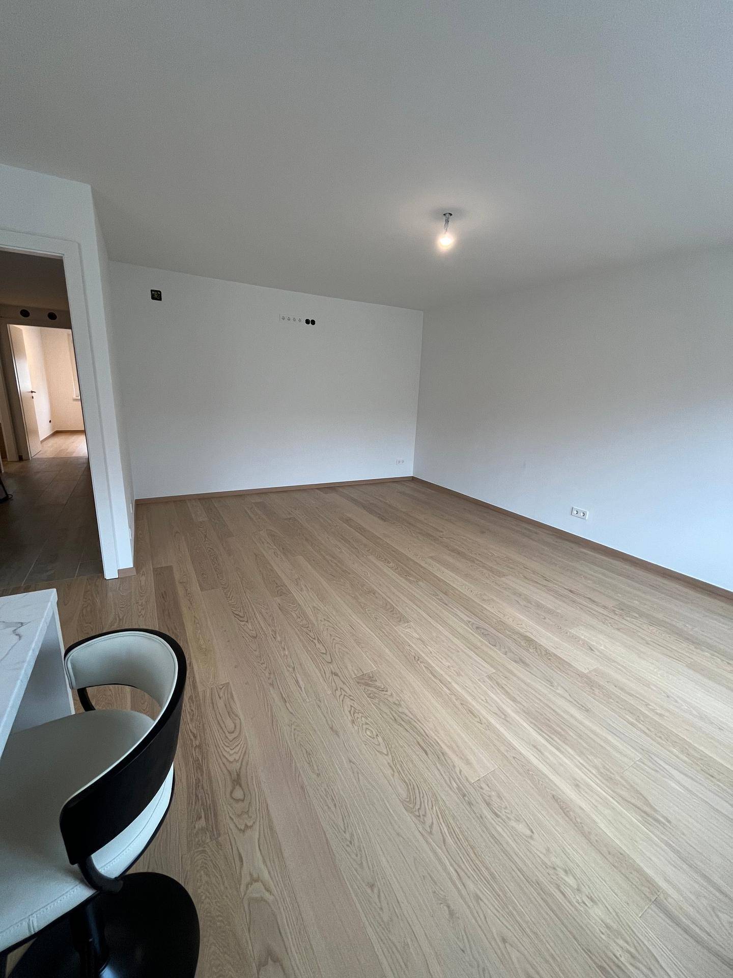 Geräumiger Wohnbereich mit hellem Parkettboden und weiß gestrichenen Wänden, offen zur Küche.
