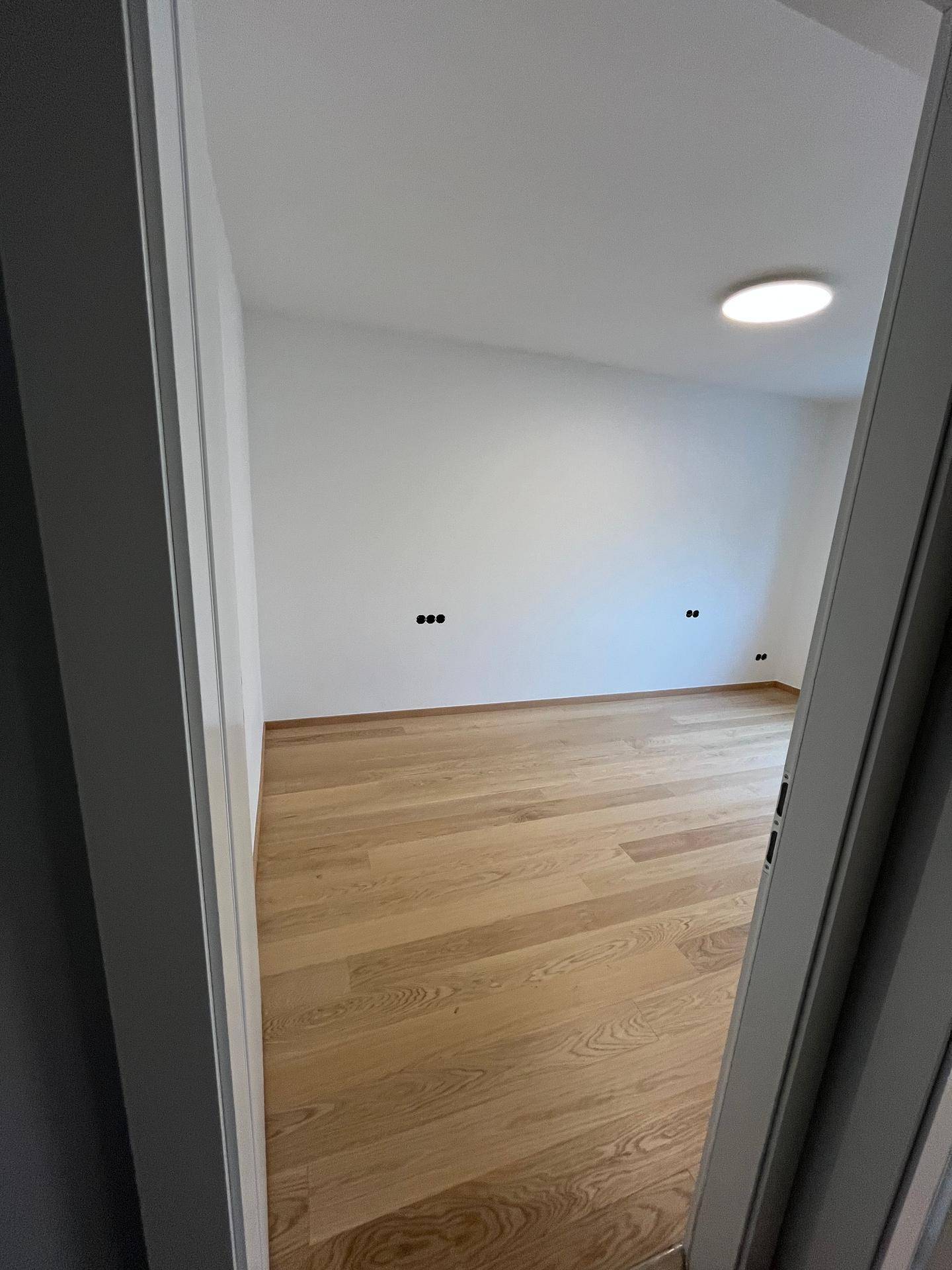 Blick durch eine Tür in ein helles Zimmer mit neuem Parkettboden und weiß gestrichenen Wänden.
