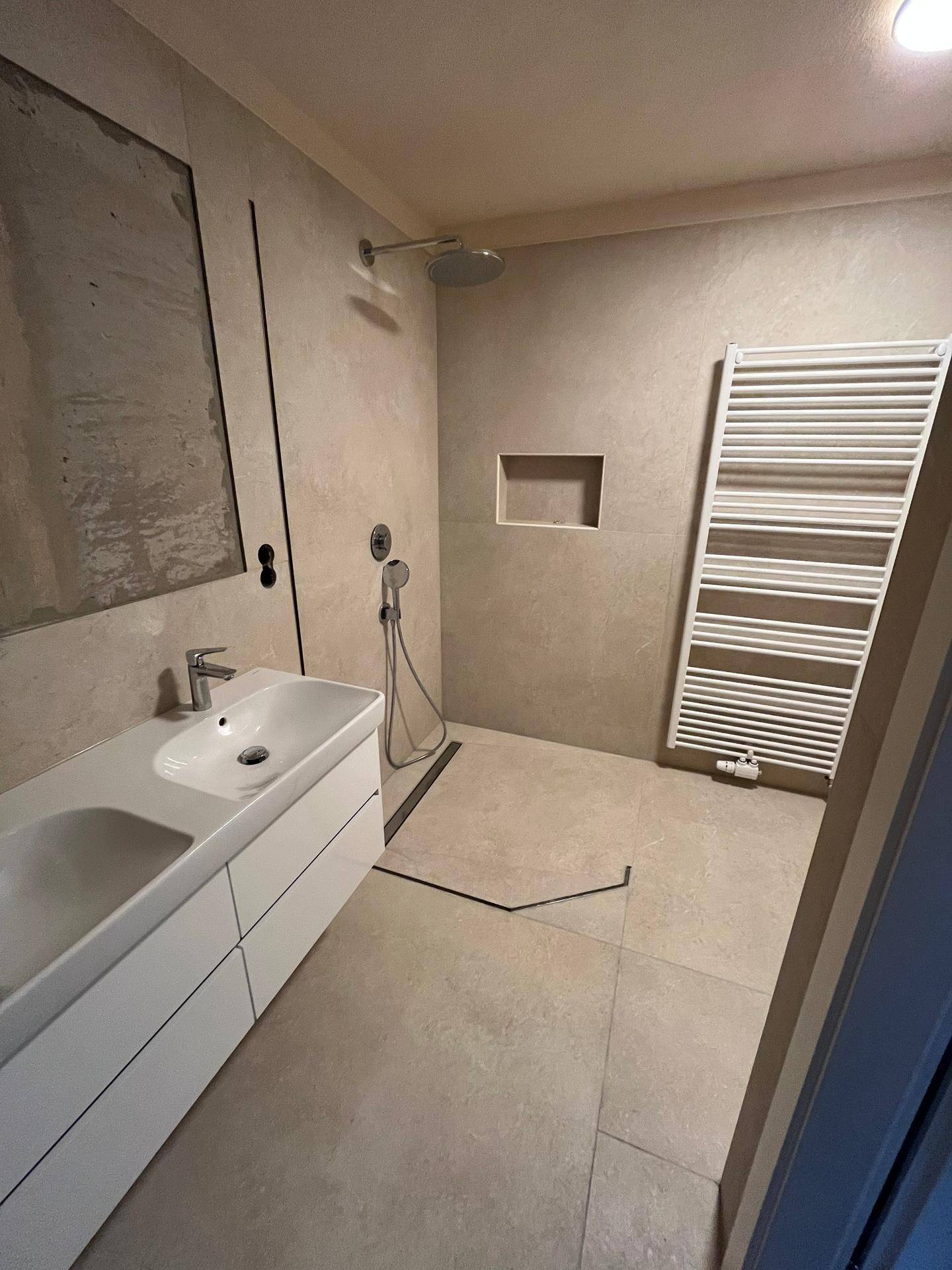 Badezimmer mit Doppelwaschbecken, ebenerdiger Dusche und beheiztem Handtuchhalter, modern und funktional.