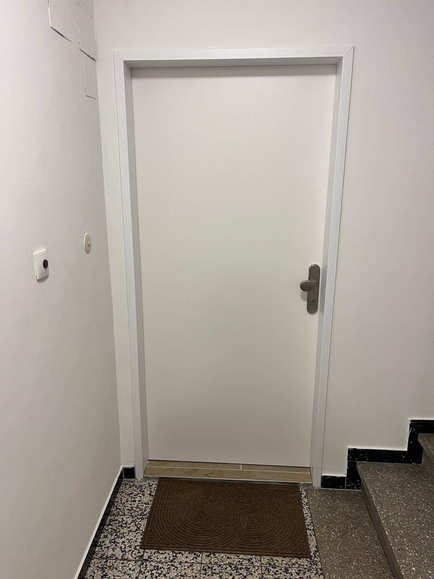 Eingangsbereich einer Wohnung mit weißer Tür und gefliestem Boden, der zu den Wohnräumen führt.
