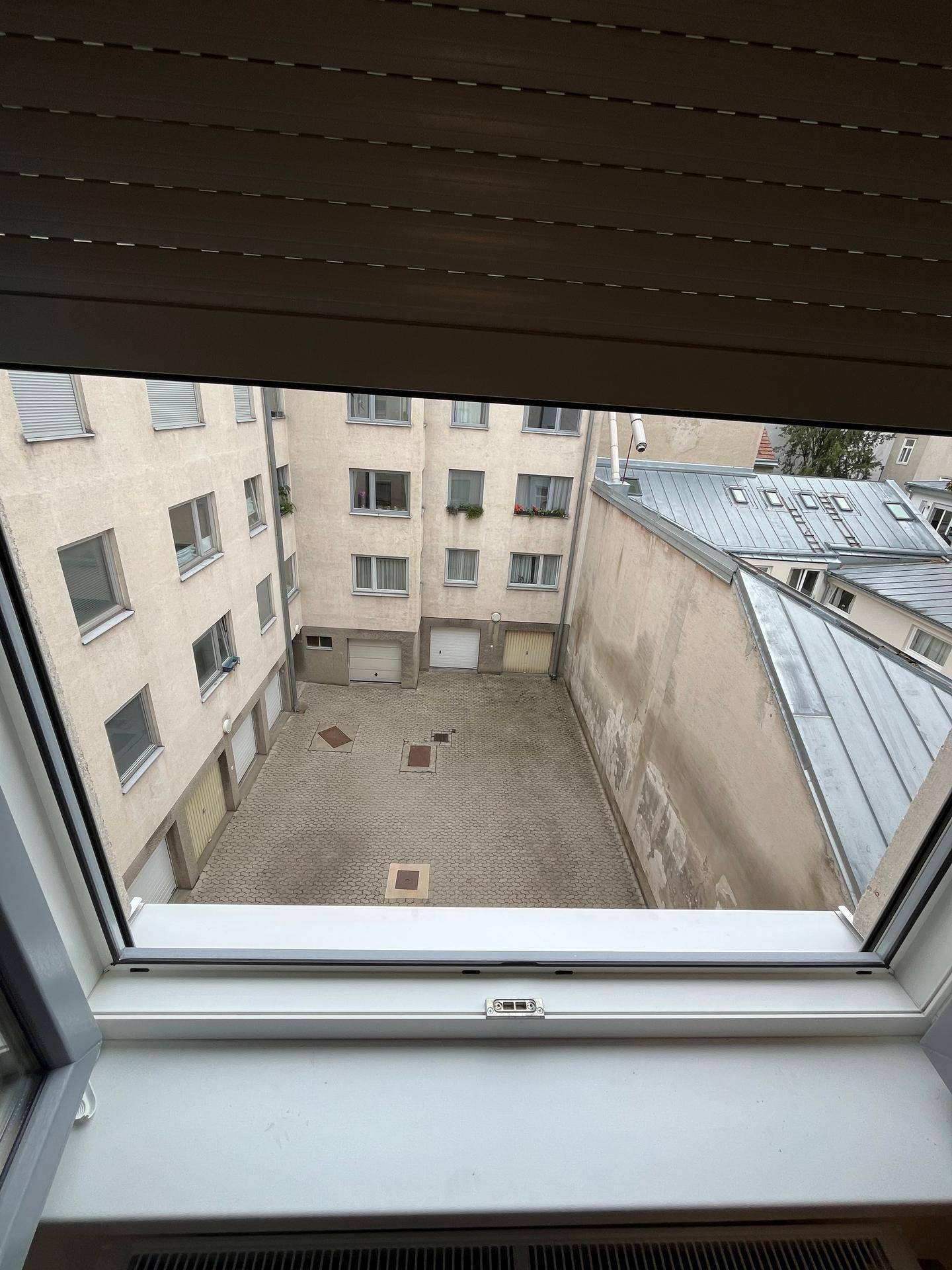Blick aus dem Fenster auf einen gepflasterten Innenhof, umgeben von Gebäuden.