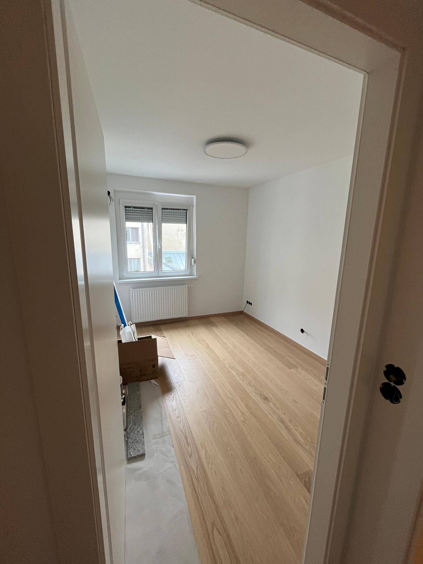 Helles Schlafzimmer mit Holzboden und Fenster, das viel natürliches Licht hereinlässt.
