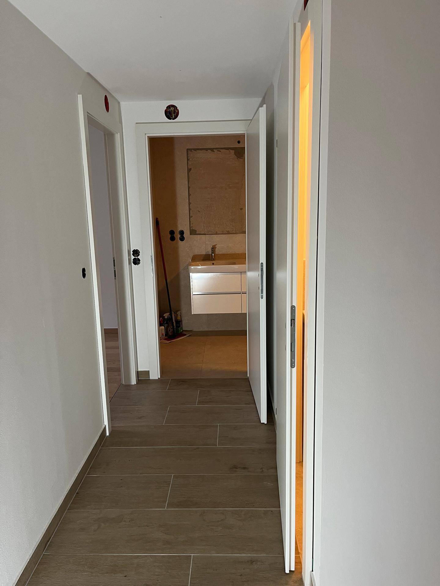 Flur mit Fliesenboden, der den Blick auf ein Badezimmer mit Doppelwaschbecken freigibt.