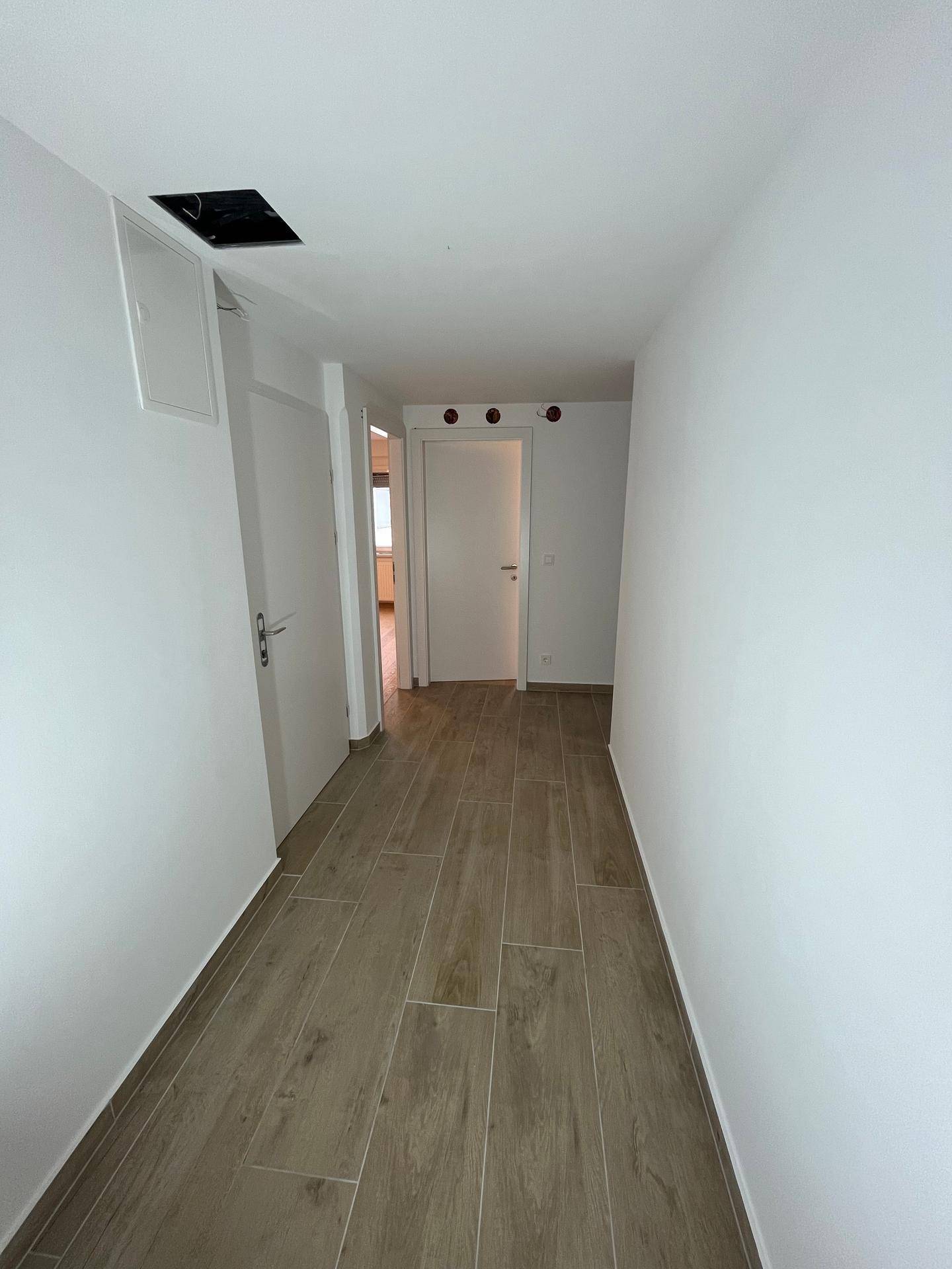 Geräumiger Flur mit Fliesenboden und weißen Wänden, der zu weiteren Zimmern führt.