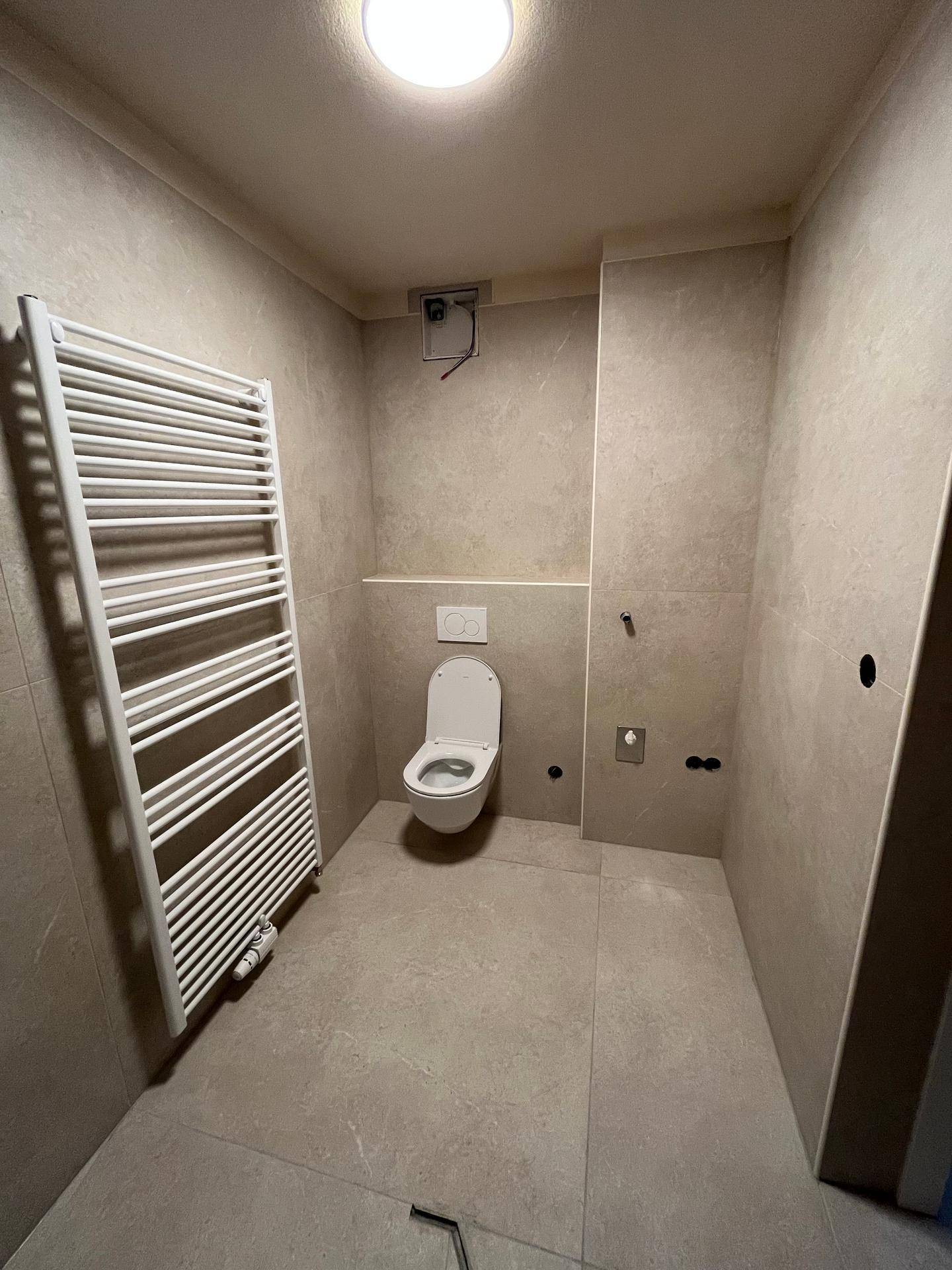Badezimmer mit wandhängender Toilette und beheiztem Handtuchhalter, in hellen Beigetönen gefliest.