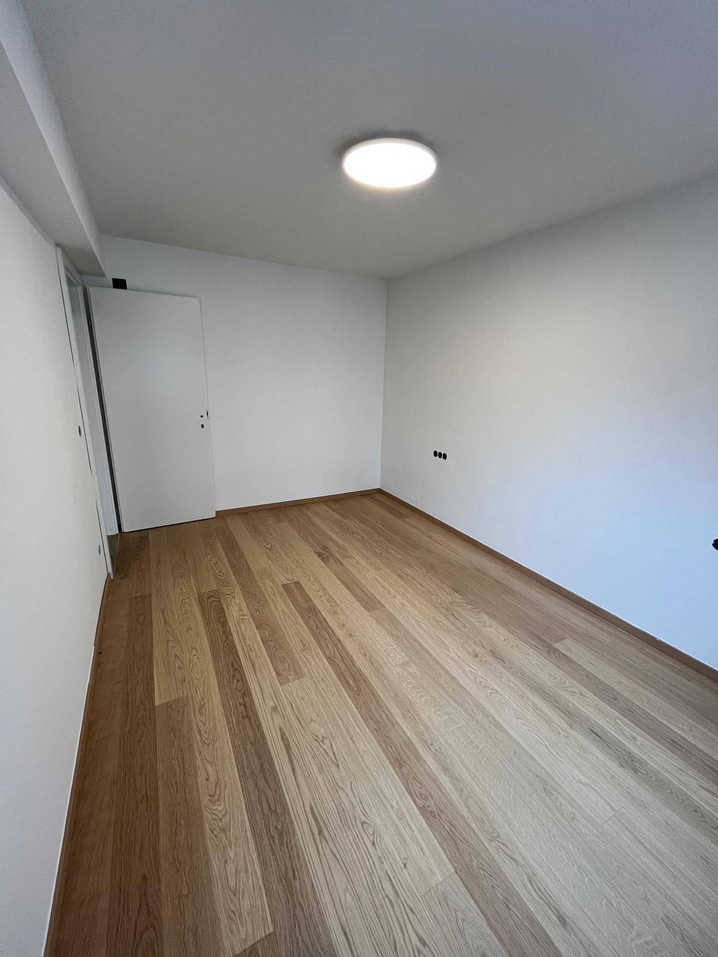 Helles Zimmer mit Parkettboden und weißer Tür, bereit für individuelle Gestaltung und Nutzung.