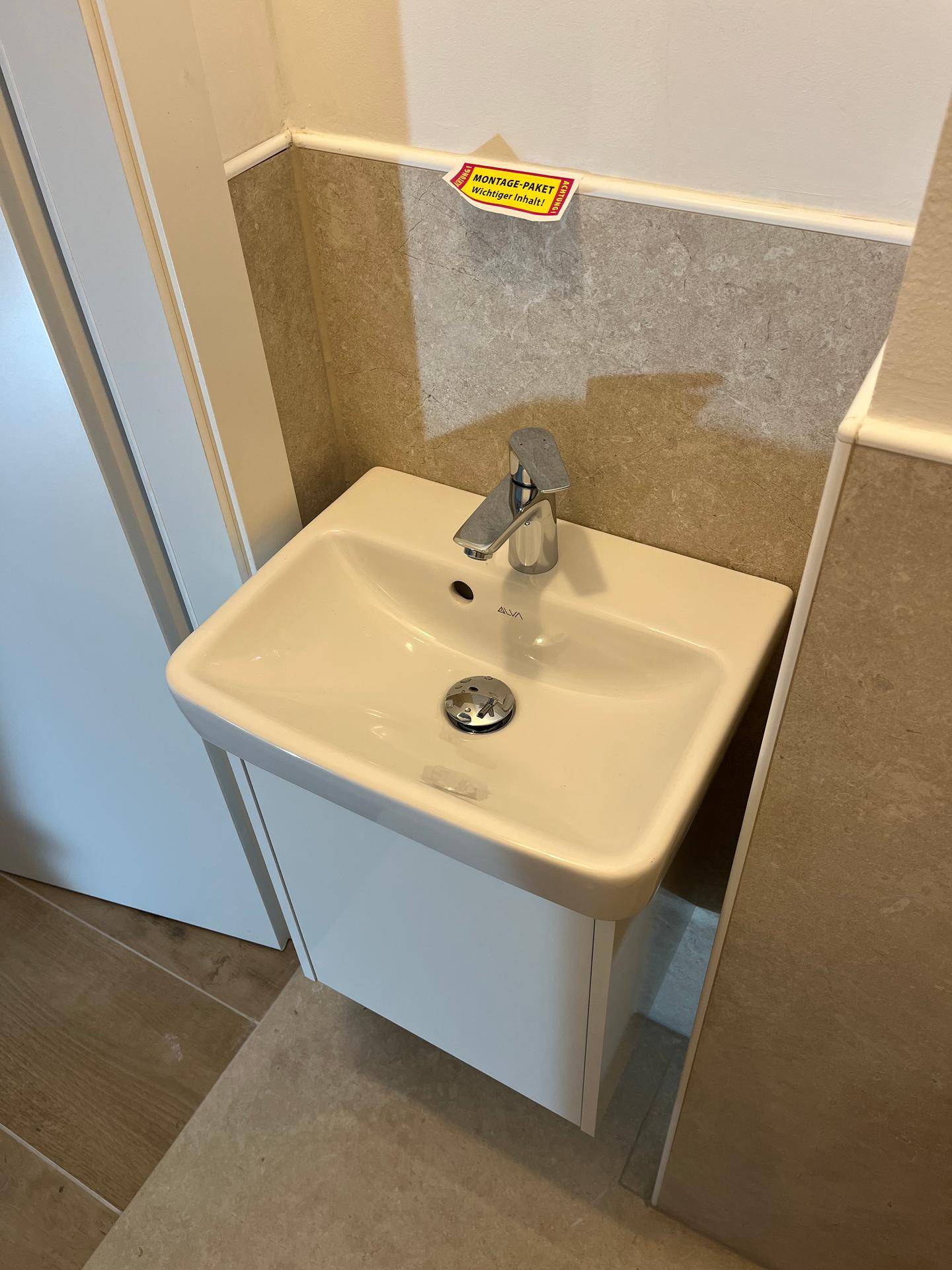 Kleines Waschbecken im Gäste-WC mit modernem Wasserhahn und hellen Fliesen.