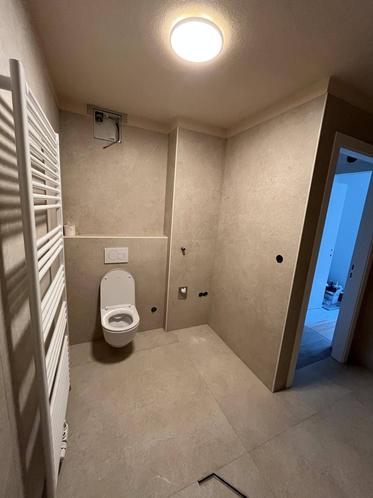 Modernes Badezimmer mit wandhängender Toilette und beheiztem Handtuchhalter, in hellen Tönen gehalten.