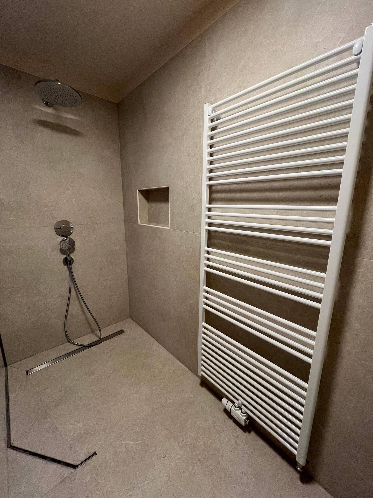 Ebenerdige Dusche mit Regenduschkopf und beheiztem Handtuchhalter in einem modernen Badezimmer.