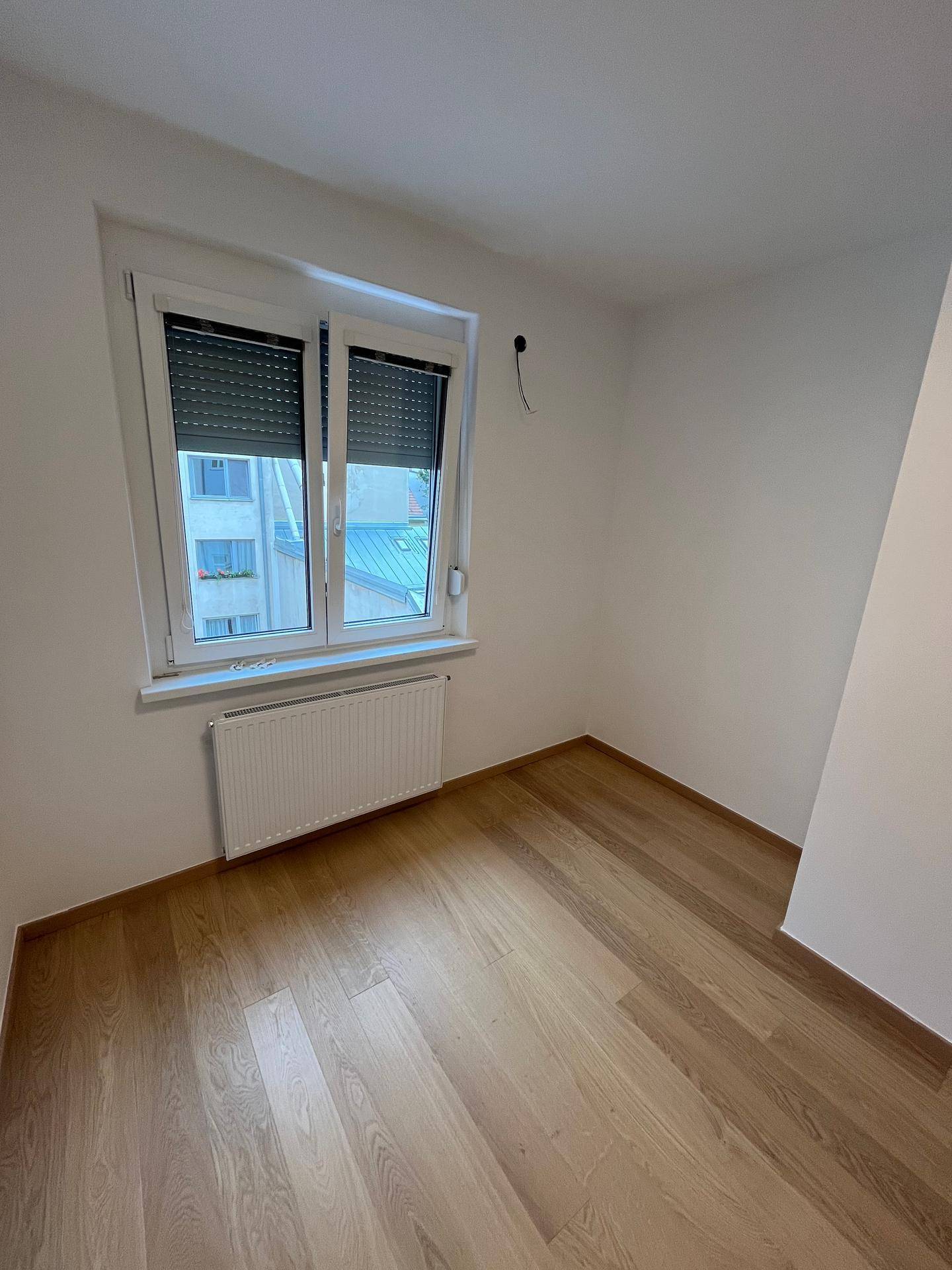 Unmöbliertes Zimmer mit Parkettboden und Fenster, das viel Tageslicht hereinlässt.