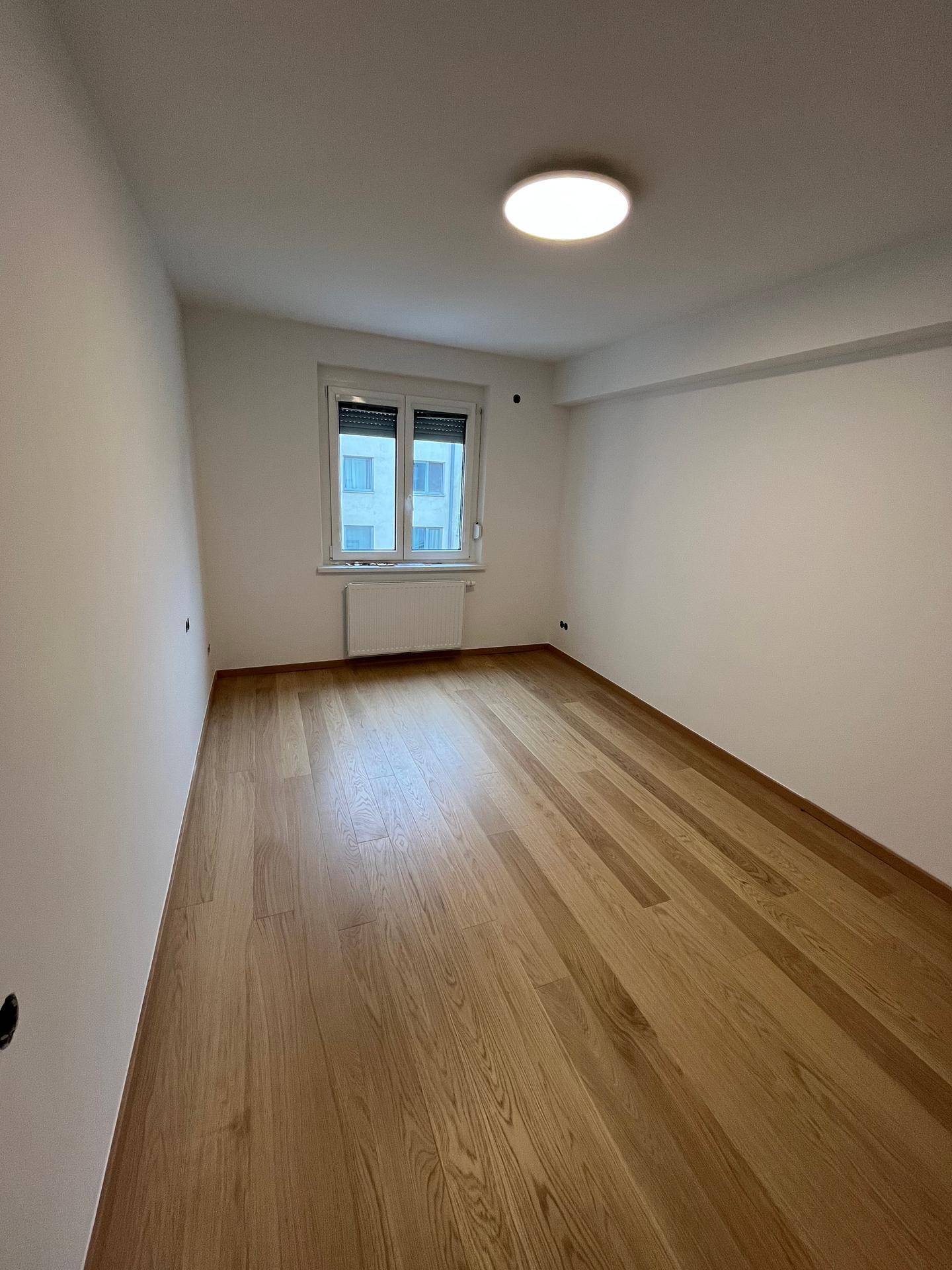 Leeres Zimmer mit Parkettboden und Fenster, das eine ruhige Atmosphäre für zukünftige Bewohner bietet.