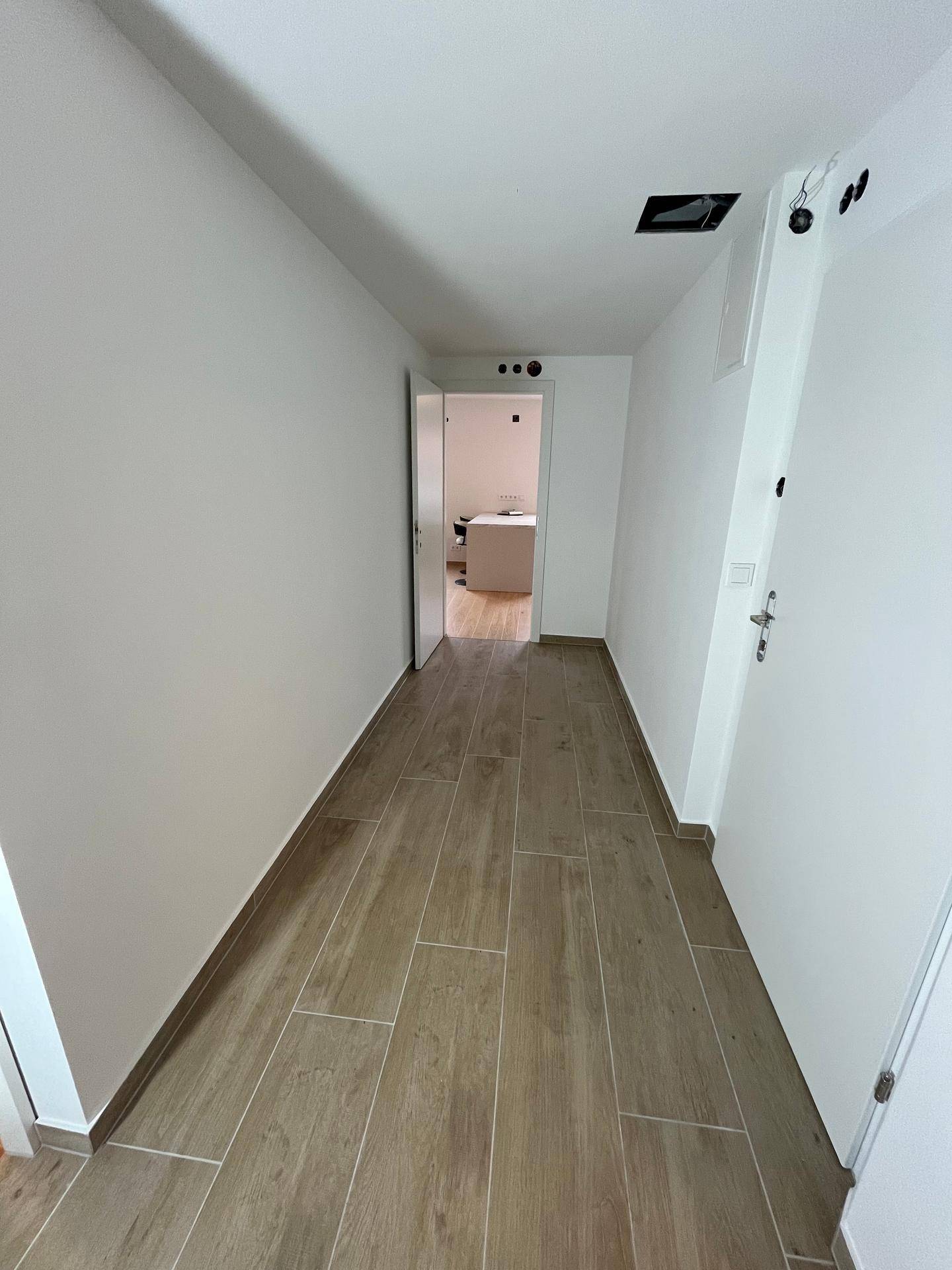 Langer, heller Flur mit Fliesenboden in Holzoptik, der einen modernen Übergang schafft.