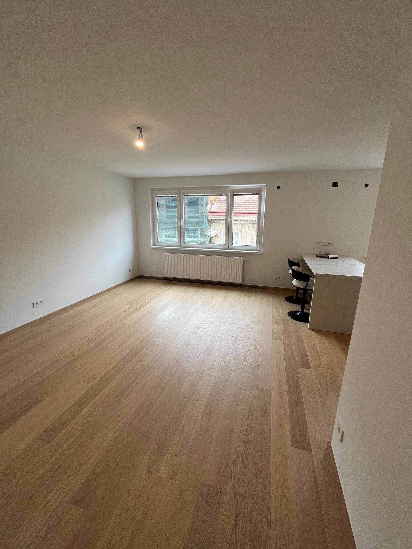 Offener Wohn- und Essbereich mit Parkettboden, Fenster und moderner Kücheninsel im Hintergrund.