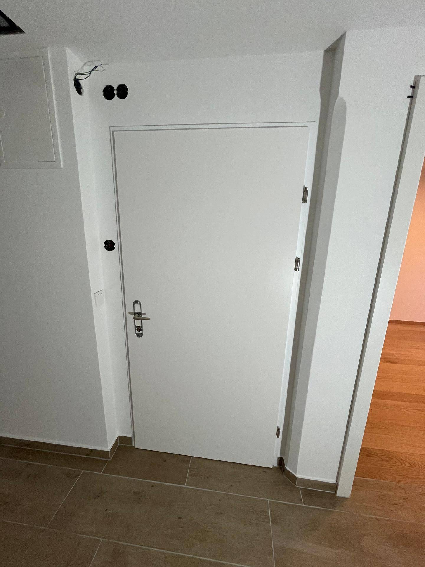 Heller Flur mit weißer Tür und Fliesenboden, der zu den verschiedenen Räumen der Wohnung führt.