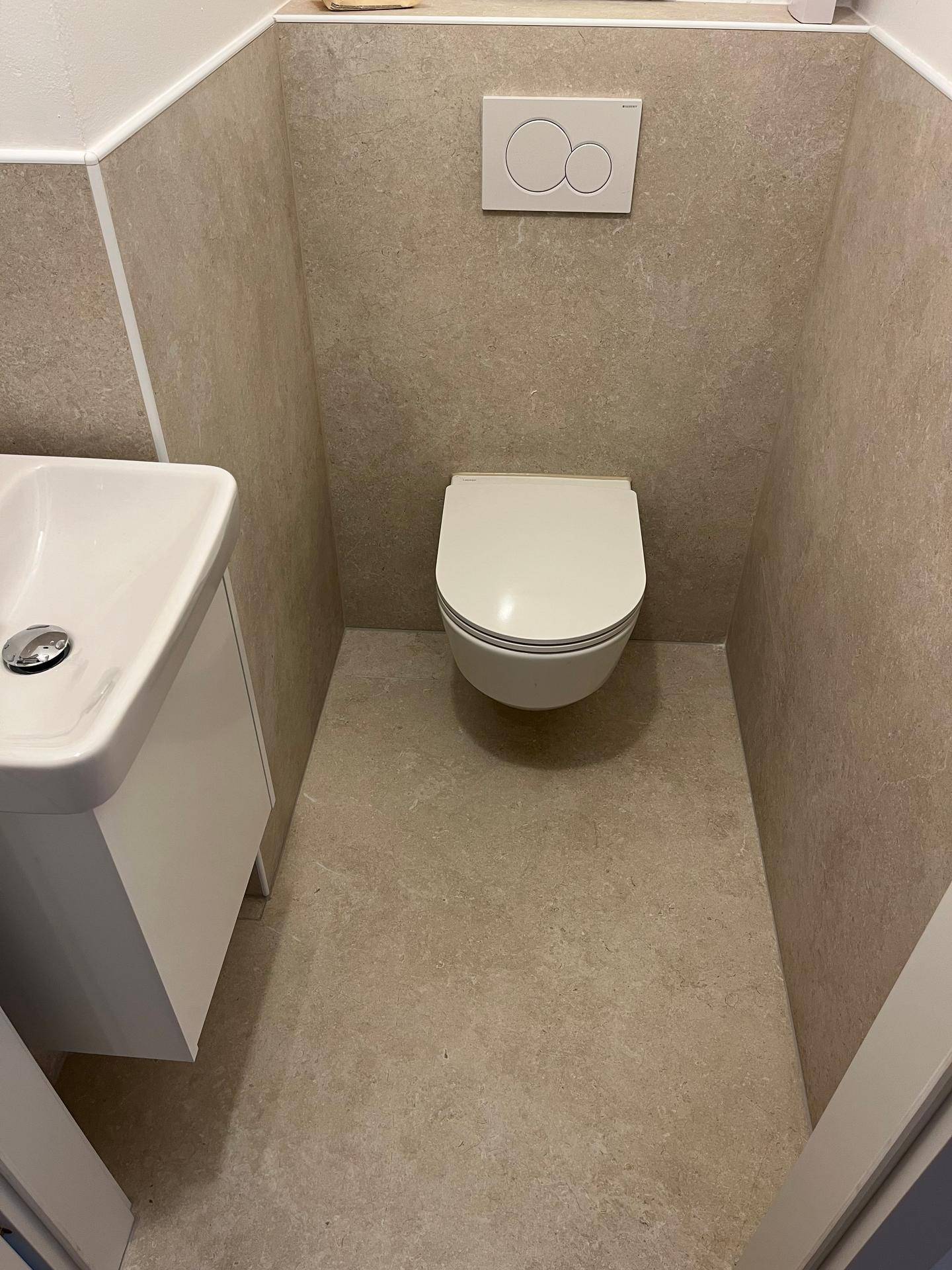 Nahaufnahme eines Gäste-WCs mit wandhängender Toilette und beigefarbenen Fliesen.