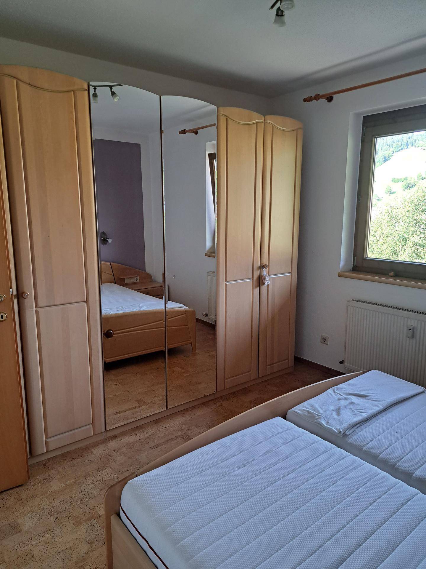 Helles Schlafzimmer mit zwei Einzelbetten, großem Spiegelschrank und Blick ins Grüne.