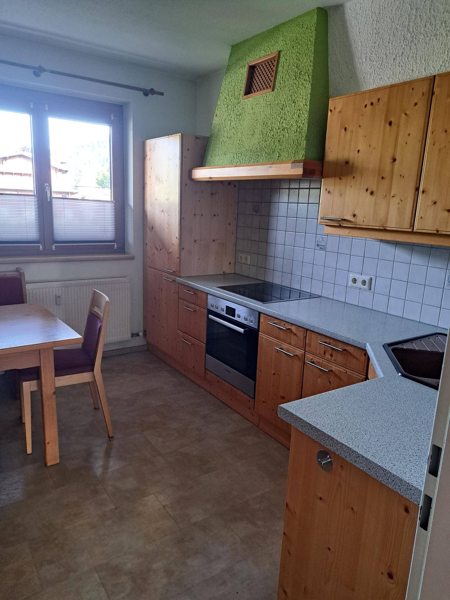 Rustikale Küche mit Holzschränken, integriertem Backofen und Essbereich am Fenster.