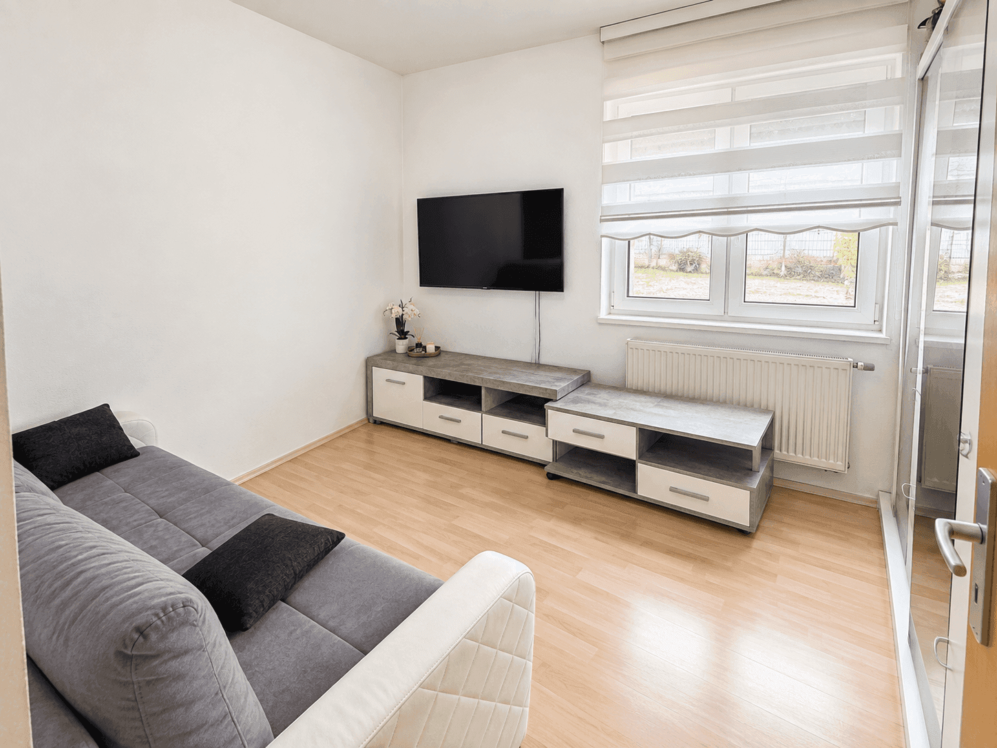 Helles Schlafzimmer mit Sofa, Fernseher und Blick ins Grüne durch das Fenster.