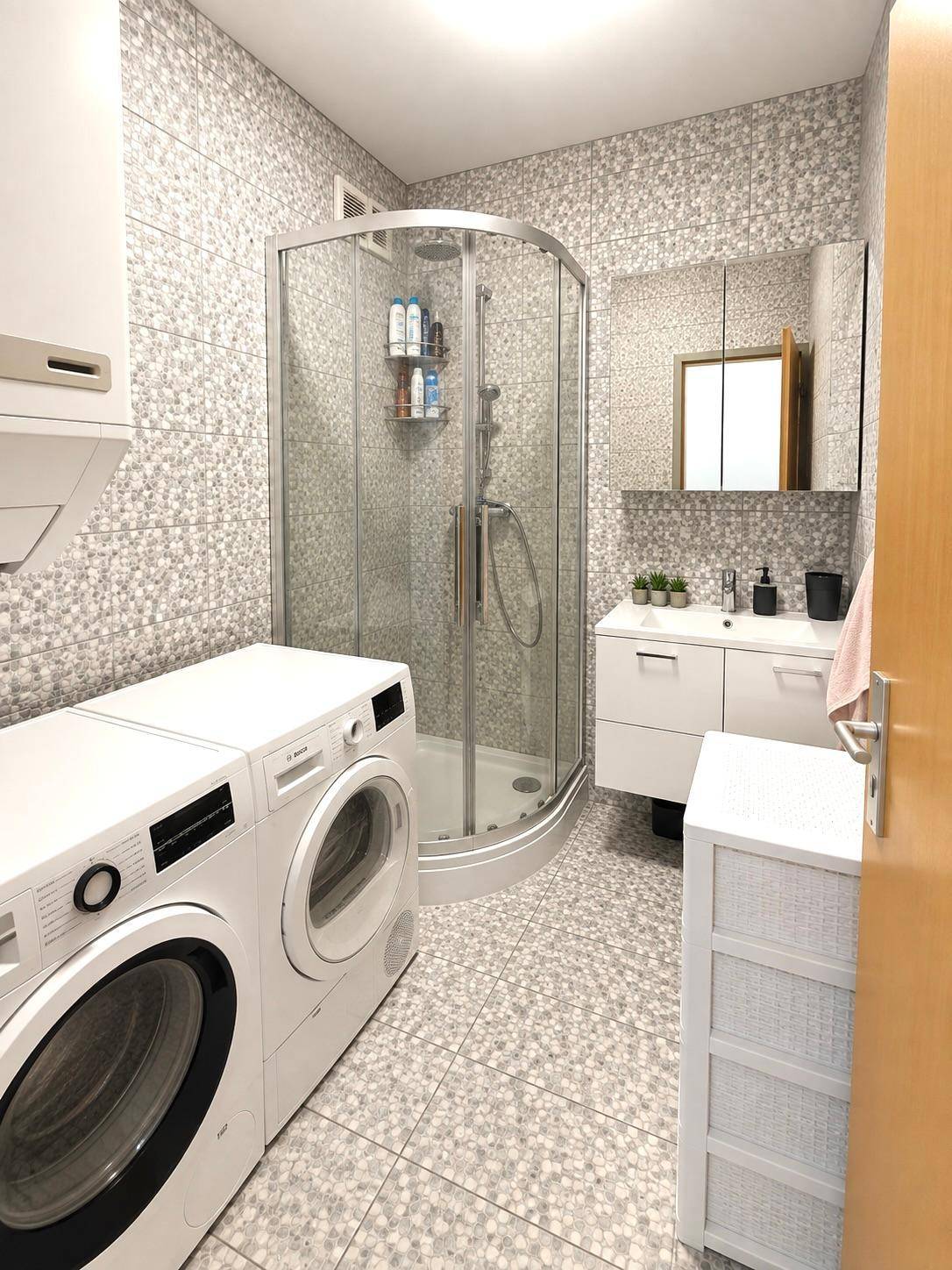 Funktionales Badezimmer mit Duschkabine, Waschmaschine, Trockner und modernen Fliesen.
