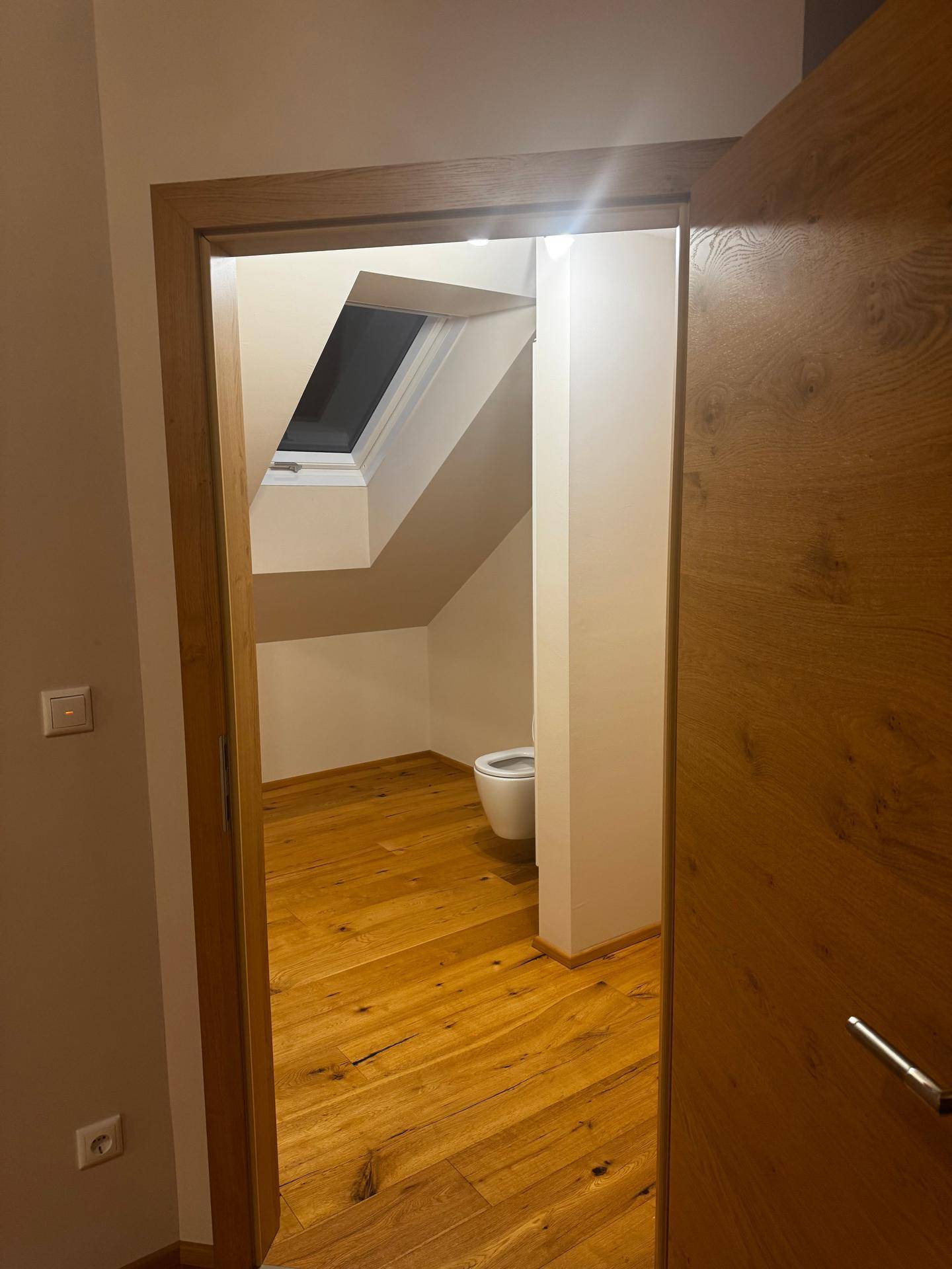 Separates WC im Dachgeschoss mit Holzboden und Dachfenster für natürliches Licht.