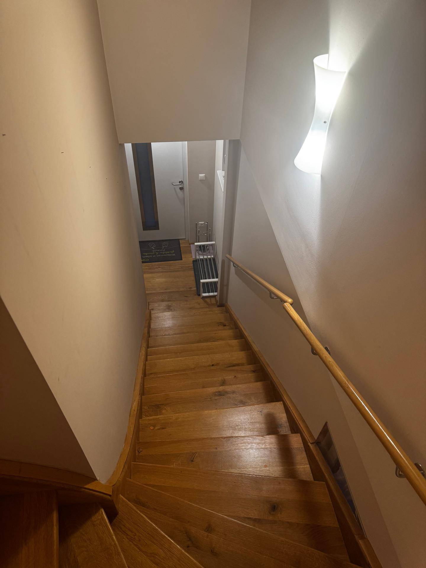 Holztreppe mit Handlauf, die zu einem unteren Bereich führt, beleuchtet von einer Wandleuchte.