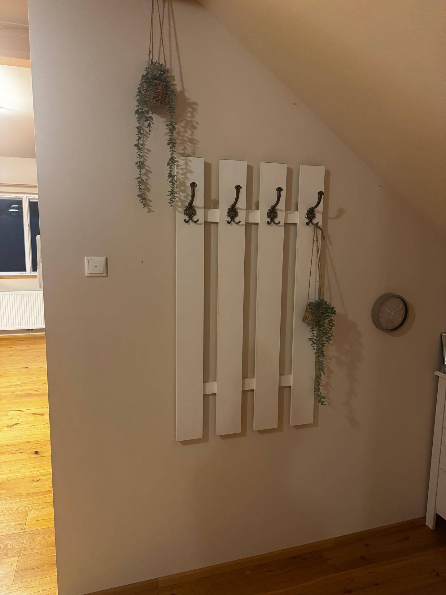 Flur mit weißer Garderobe, dekorativen Hängepflanzen und Holzboden.