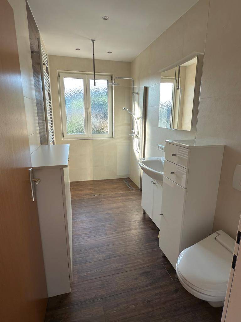 Modernes Badezimmer mit dunklem Fliesenboden, Fenster und weißem Waschtischunterschrank.