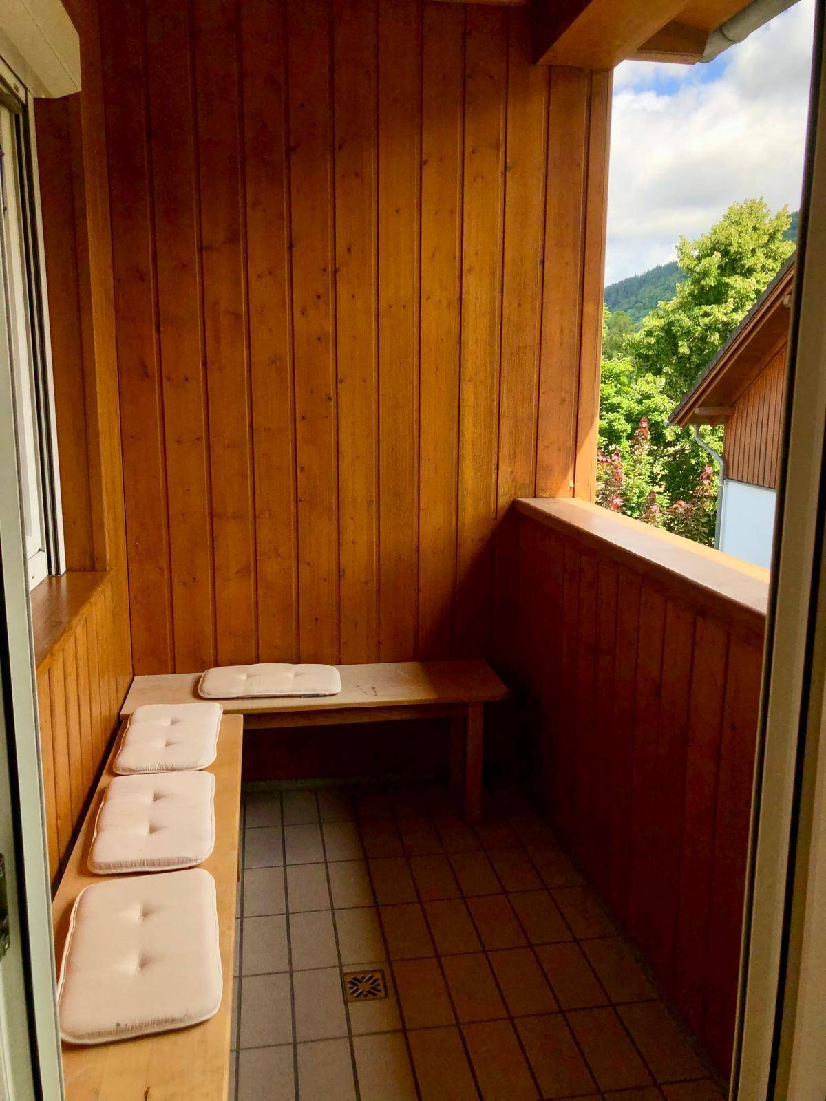 Gemütlicher Holzbalkon mit integrierten Sitzgelegenheiten und Blick ins Grüne.
