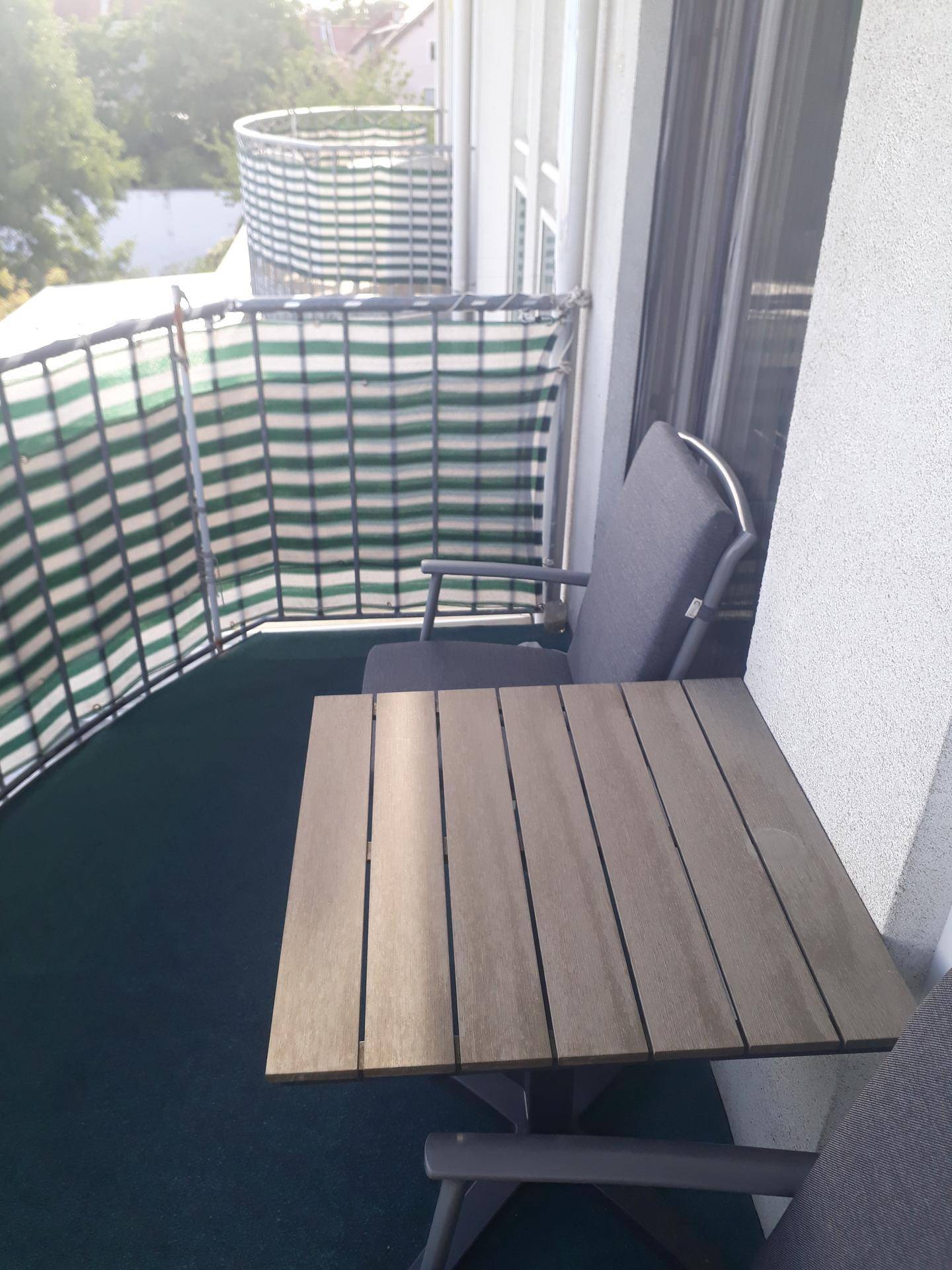 Weiterer Blick auf den Balkon mit Tisch, Stühlen und grün-weißem Sichtschutz.
