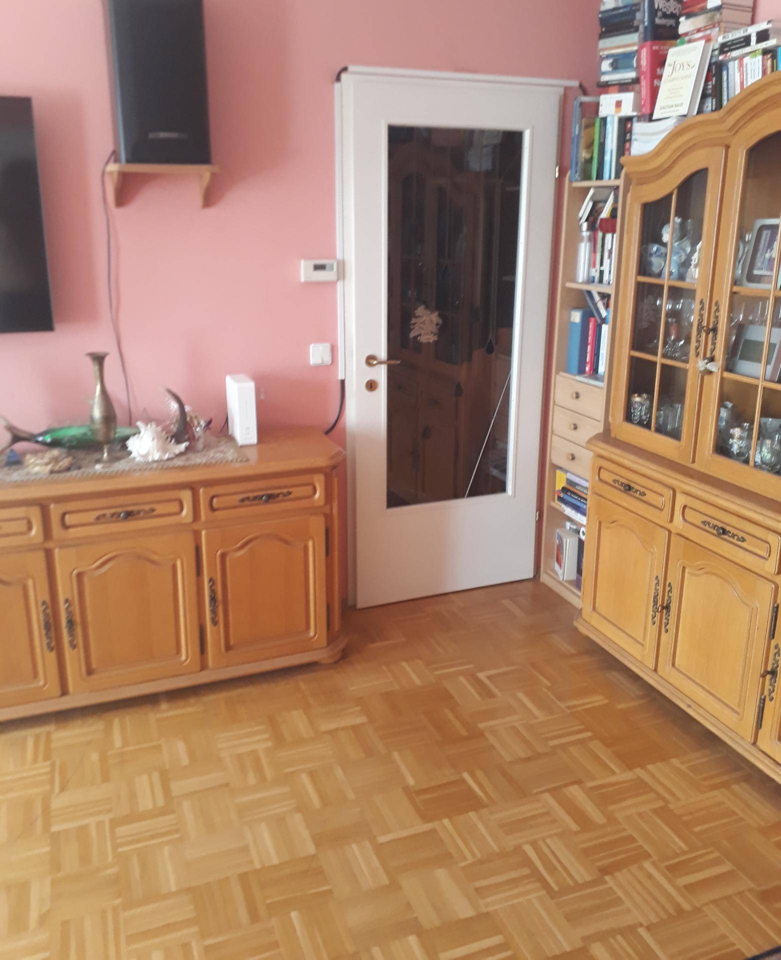 Wohnzimmerbereich mit traditionellen Holzmöbeln, Bücherregal und einer Tür mit Glaseinsatz.