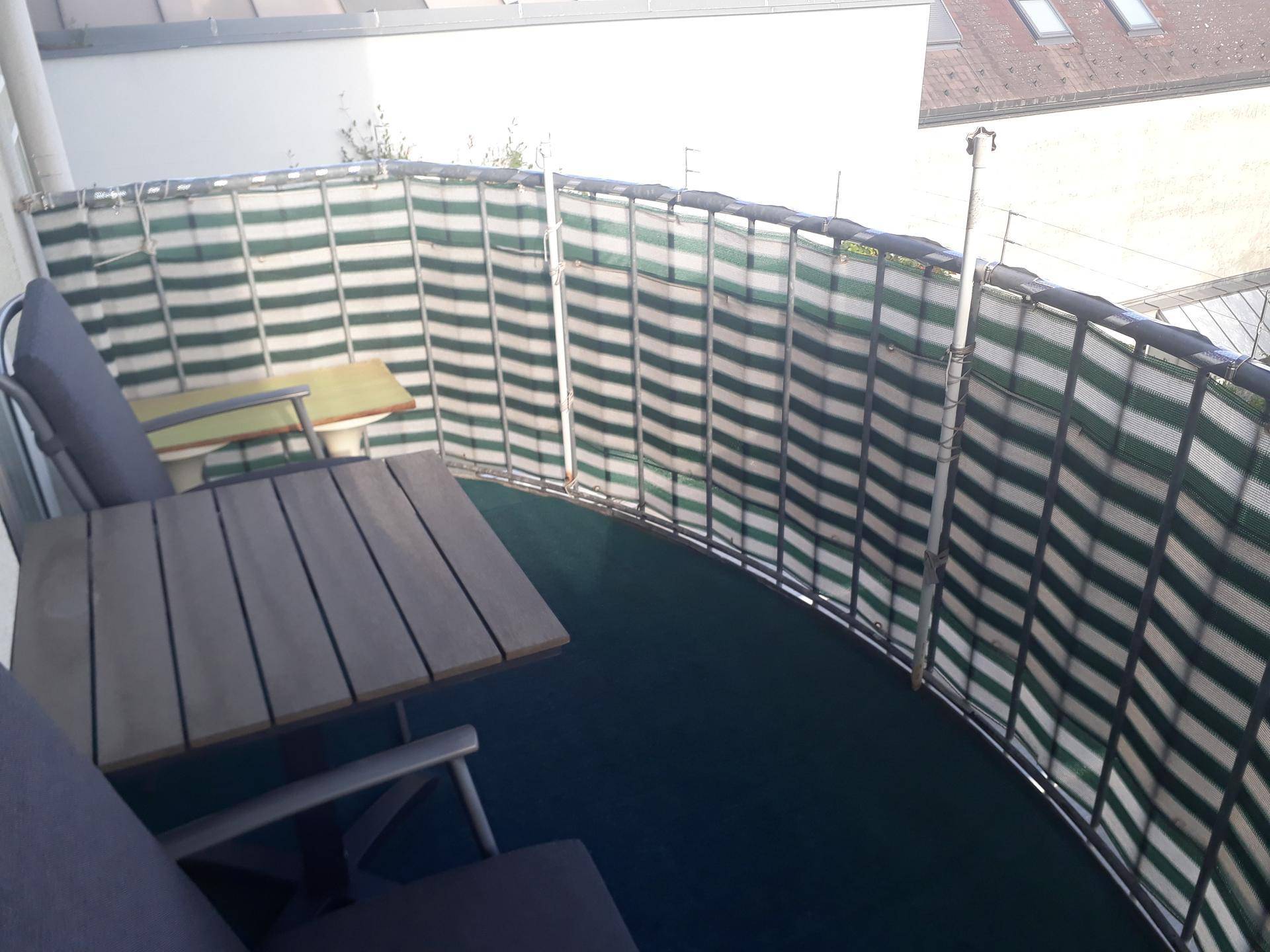 Balkon mit Gartenmöbeln und einem grün-weiß gestreiften Sichtschutz für Privatsphäre.