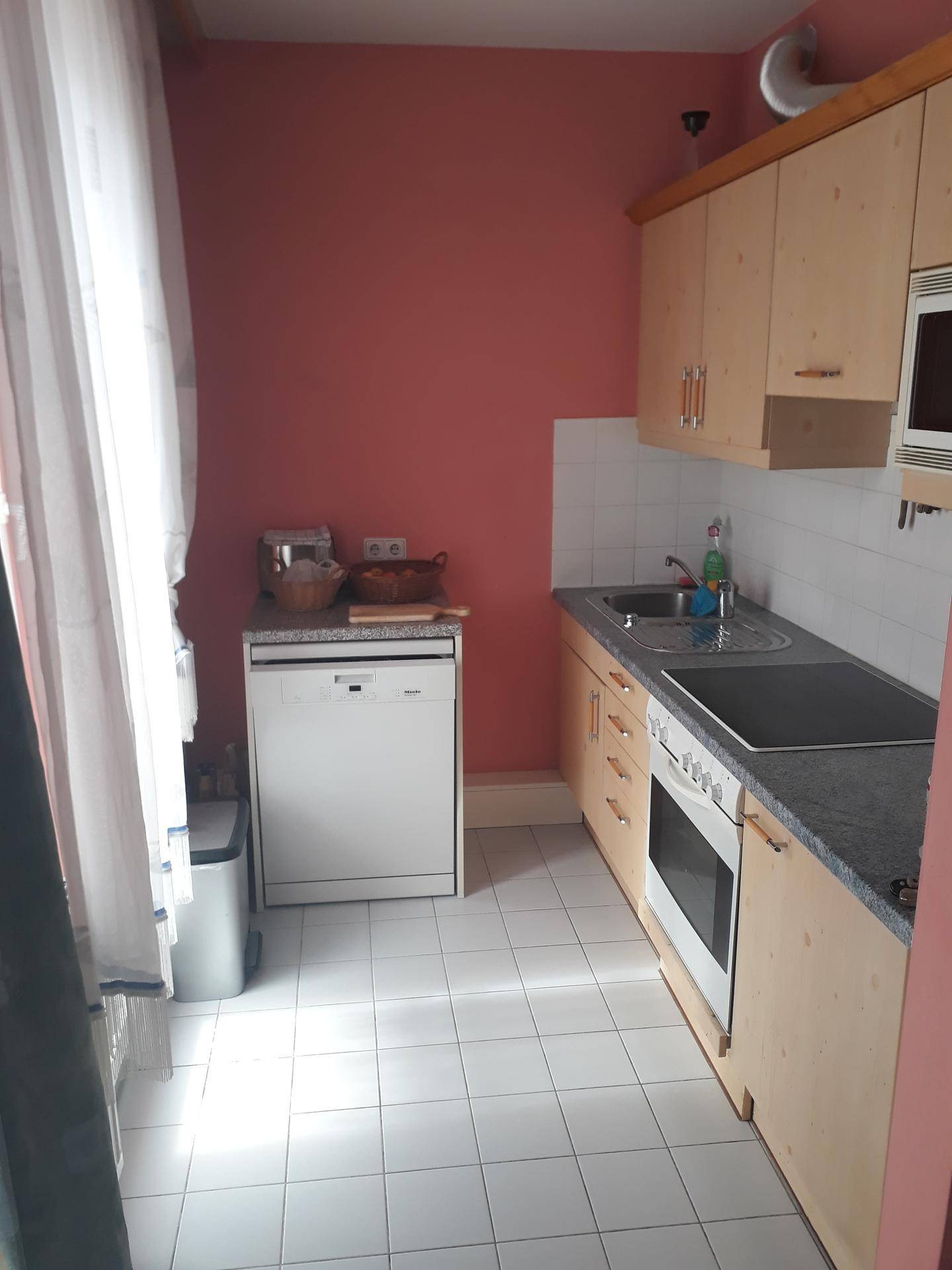 Schmale Küche mit hellen Holzschränken, weißem Fliesenspiegel und integrierten Geräten.