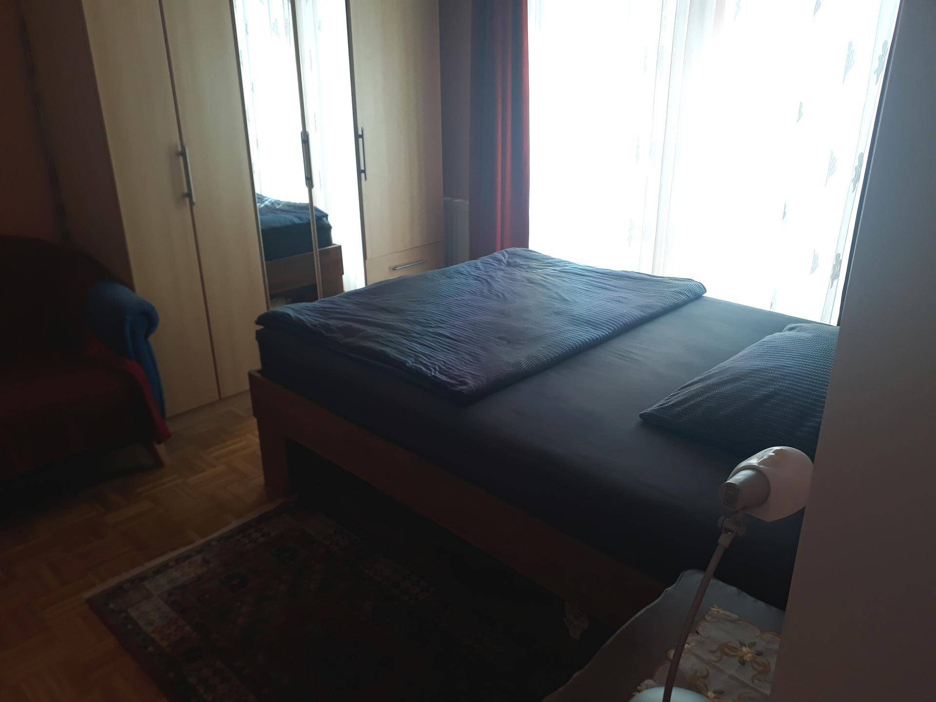 Helles Schlafzimmer mit Doppelbett, Kleiderschrank und großen Fenstern für viel Tageslicht.