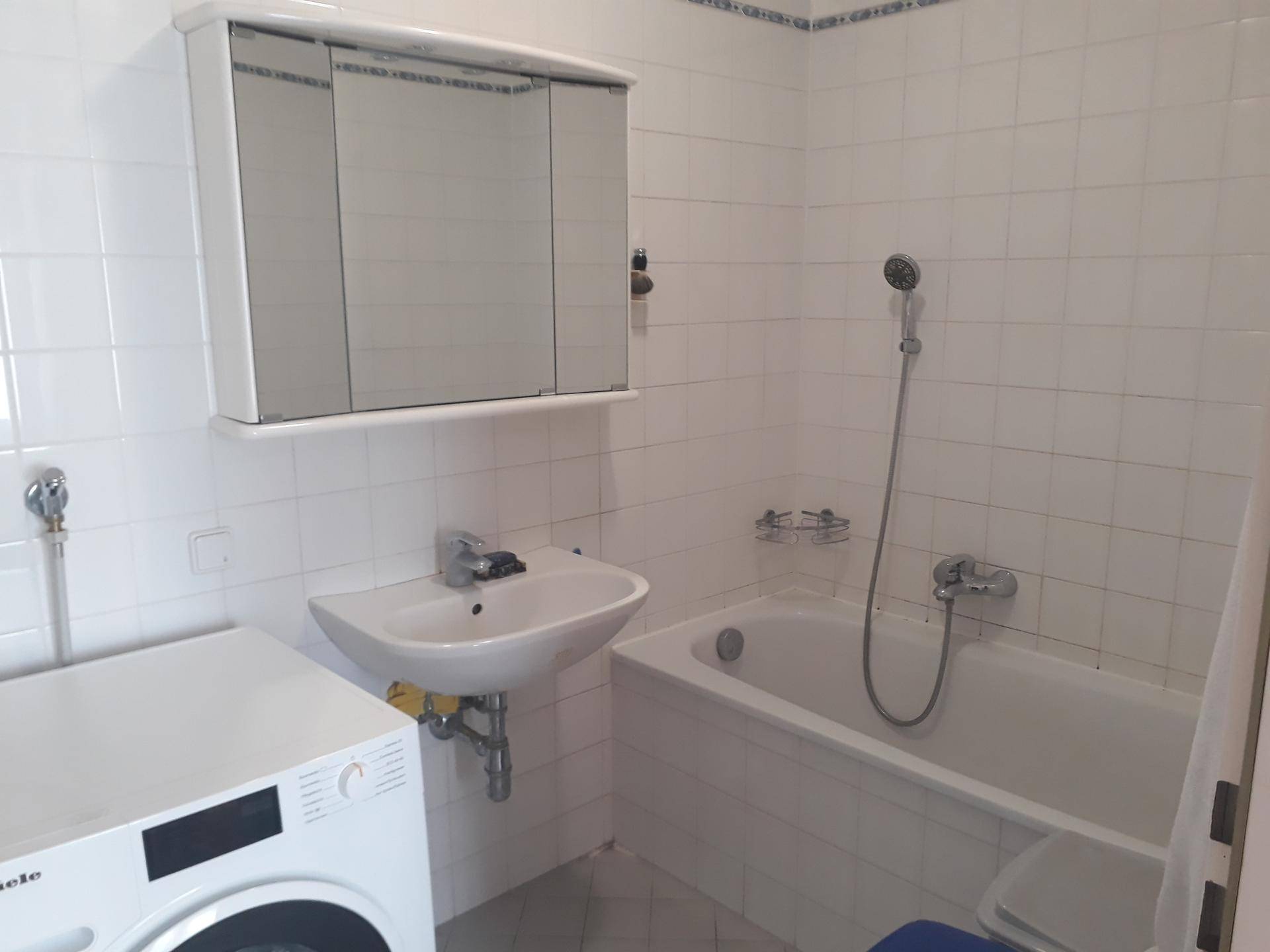 Badezimmer mit Badewanne, Waschbecken, Spiegelschrank und einer Waschmaschine.