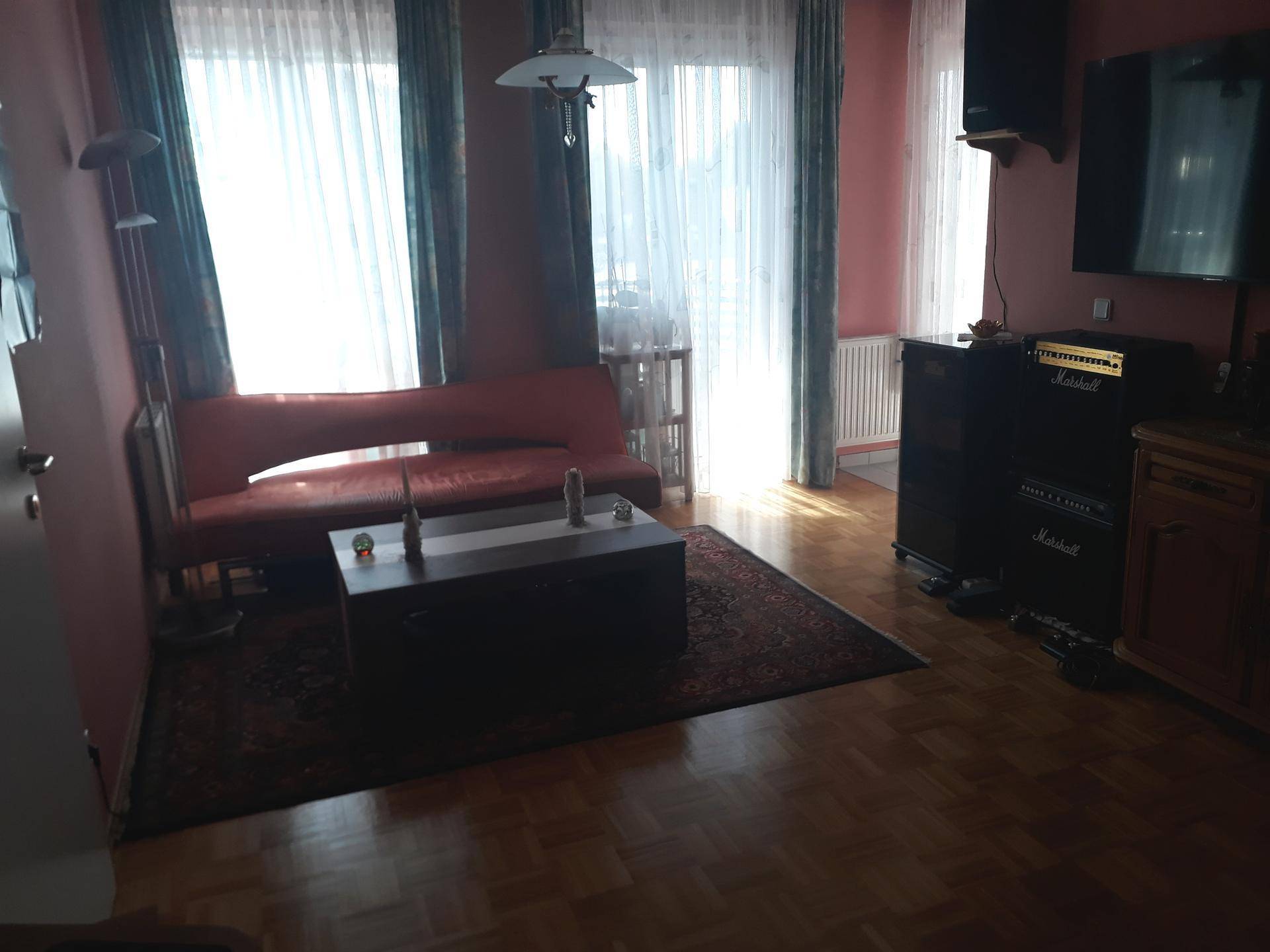 Gemütliches Wohnzimmer mit rotem Sofa, Holzboden und hellem Zugang zu einem Außenbereich.